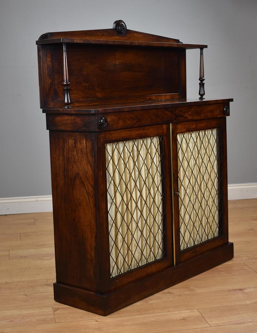 Victorian rosewood chiffonier in good condition with top shelf supported by delicate turned columns with two cupboard doors with brass grills, the fabric can be easily removed or replaced, the chiffonier stands on plinth base.