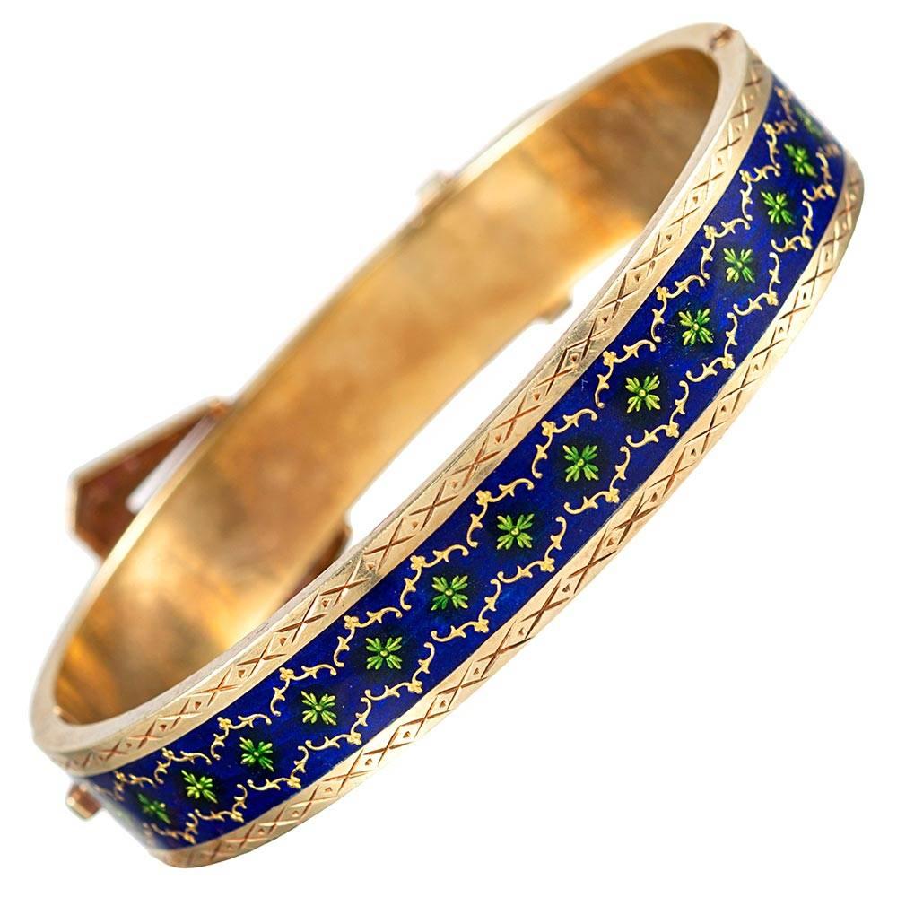 Buckle motif jewelry was popularized by Queen Victoria, as she was known to favor this theme. This 18 karat yellow gold bangle is extensively decorated with royal blue and Kelly green enamel and further complimented with seed pearls. The interior