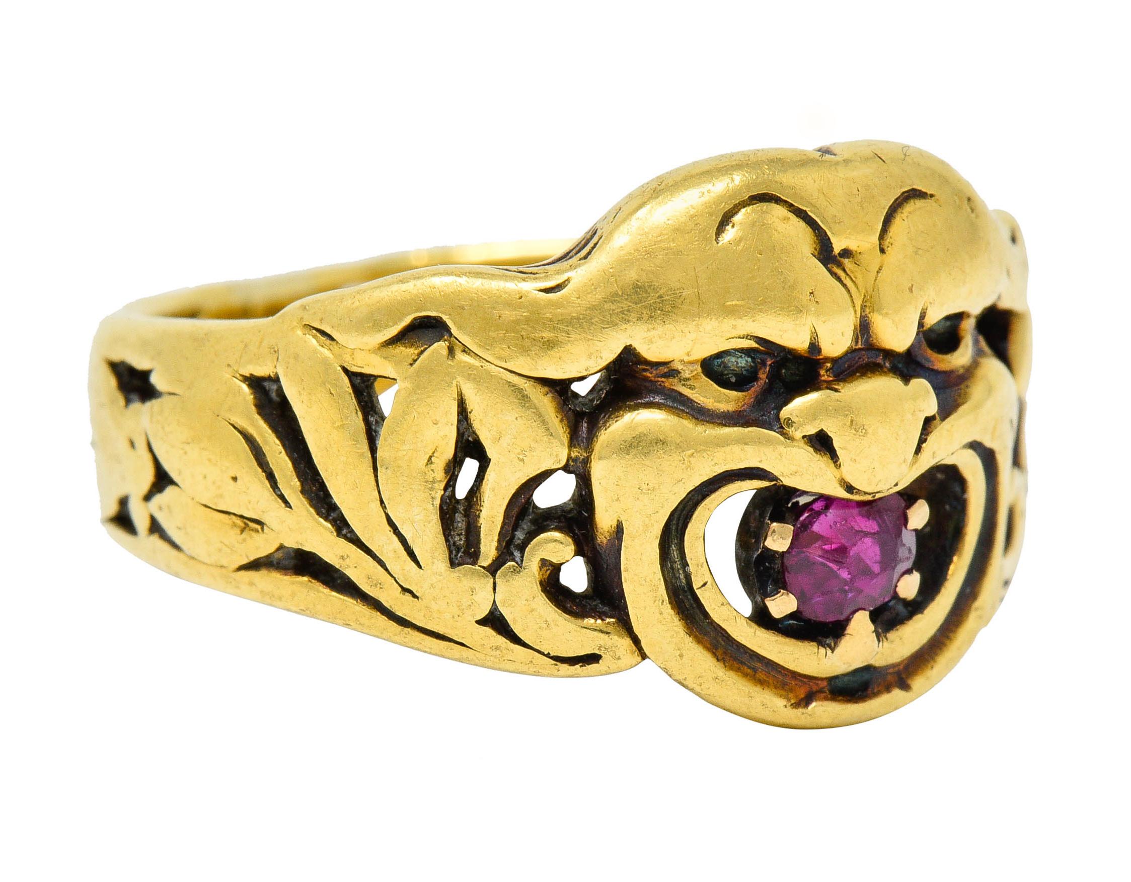 Band ring is deeply carved to depict a grimacing gargoyle face

Centering a rectangular cushion cut ruby weighing approximately 0.24 carat; bright purplish-red

Completed by pierced shoulders designed with flourishing foliate

Tested as 18 karat