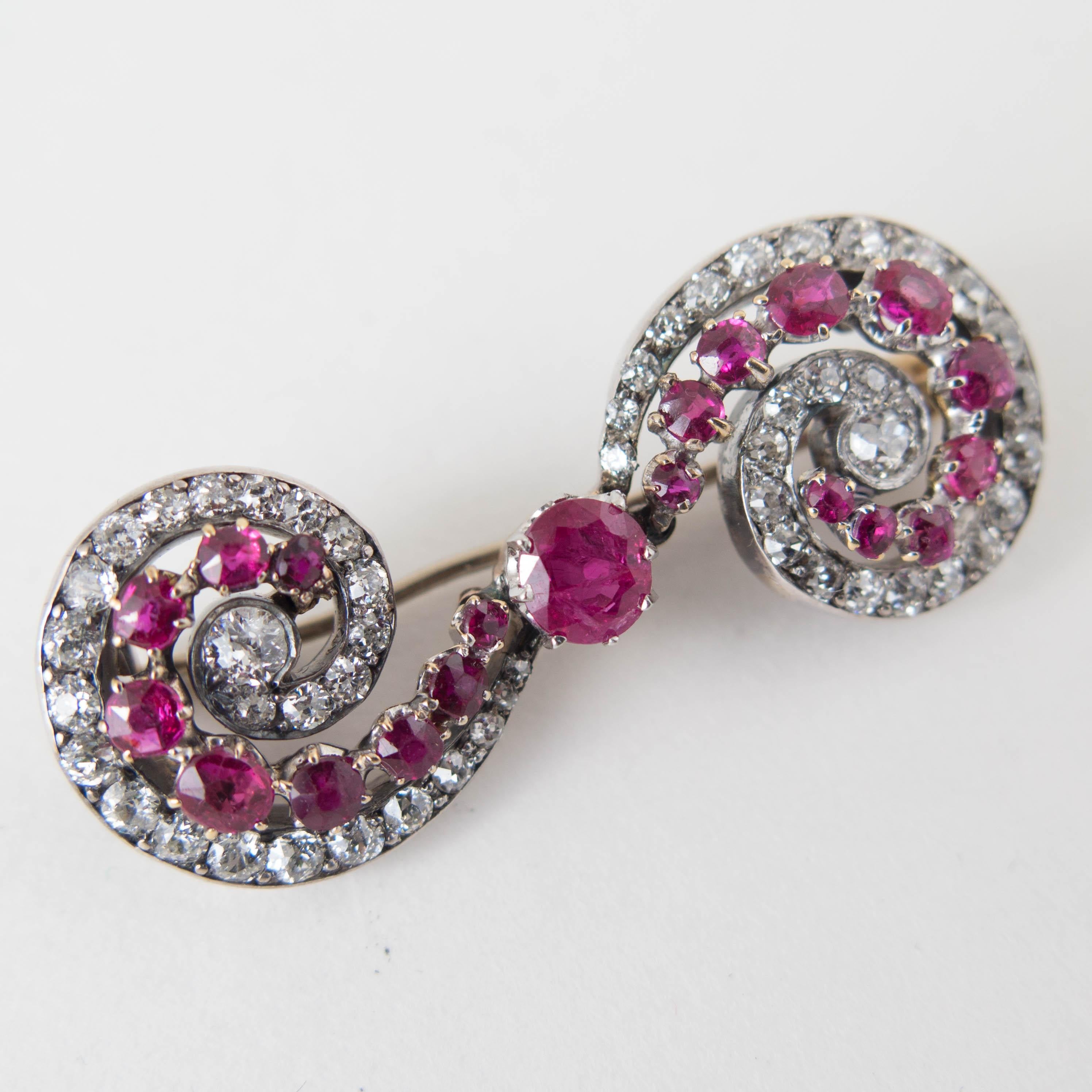 A wonderful late 19th century Victorian ruby and diamond scroll or swirl brooch set in silver topped 18k gold.

The small brooch of impeccable design, featuring two opposing swirl or scroll patterns centered around a center ruby. 

20 natural rubies