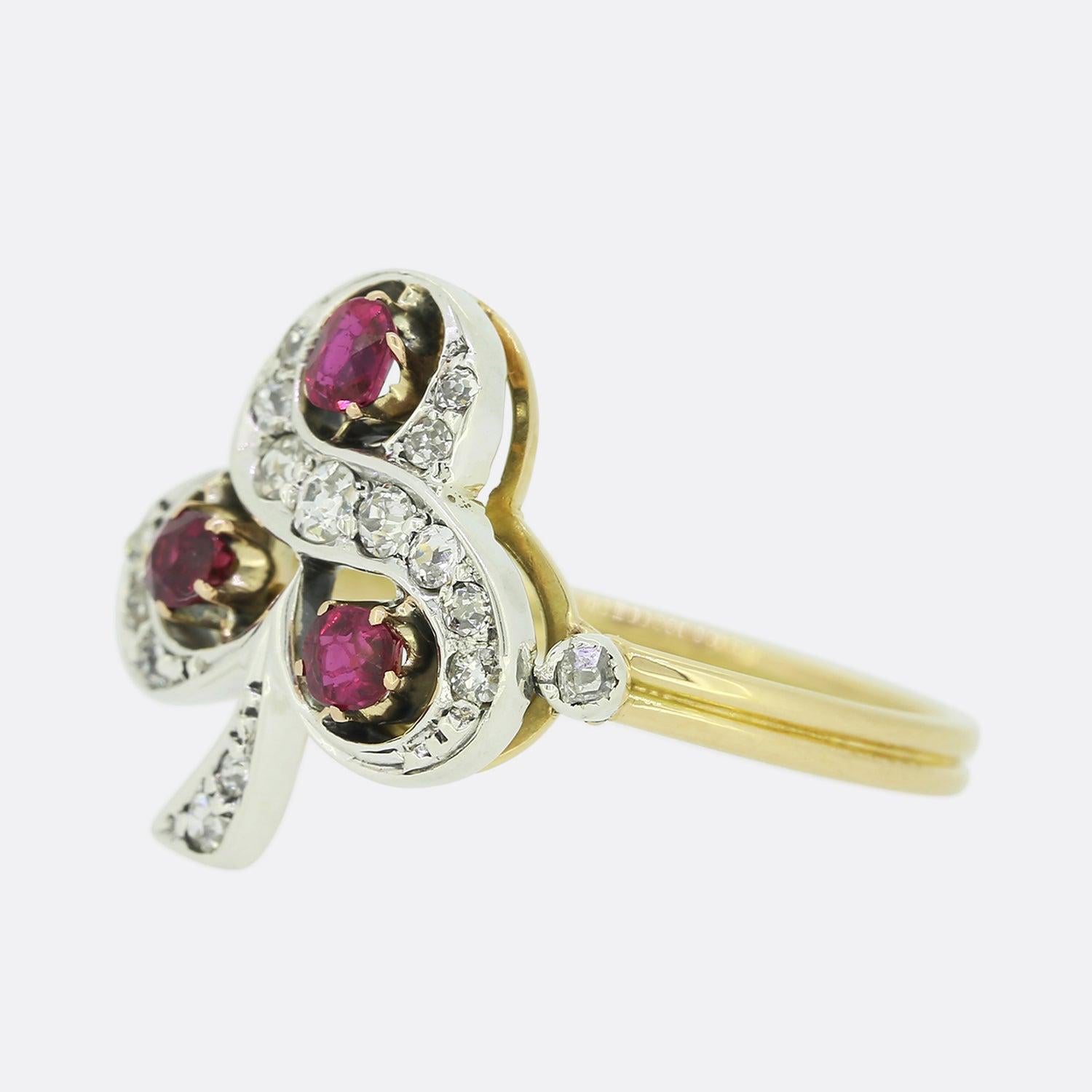 This is a charming 18ct yellow gold ruby and diamond clover ring. The ring is set with a trio of round and oval shaped rubies within an open detailed design. Crafted in platinum, the ring's clover structured face features a vast array of old cut