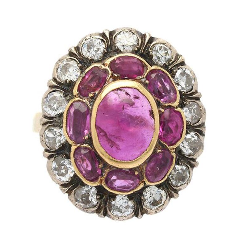 A Victorian ruby and diamond cluster ring in silver and gold, 1880s. The central ruby cabochon weighs approximately 1 carat and is clustered by facetted rubies and round old European cut diamonds. The ring has rubbed makers marks and a 14k gold