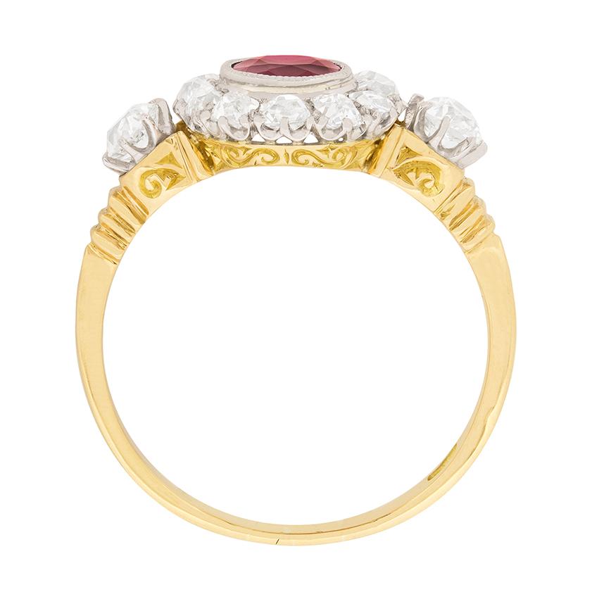 Dating to the 1900s, this Victorian ring features a deep red ruby in a rub over setting. The natural gemstone weighs 0.90 carat and is haloed by sparkling old cut diamonds. The halo has a combined weight of 0.70 carat. On either shoulder there is