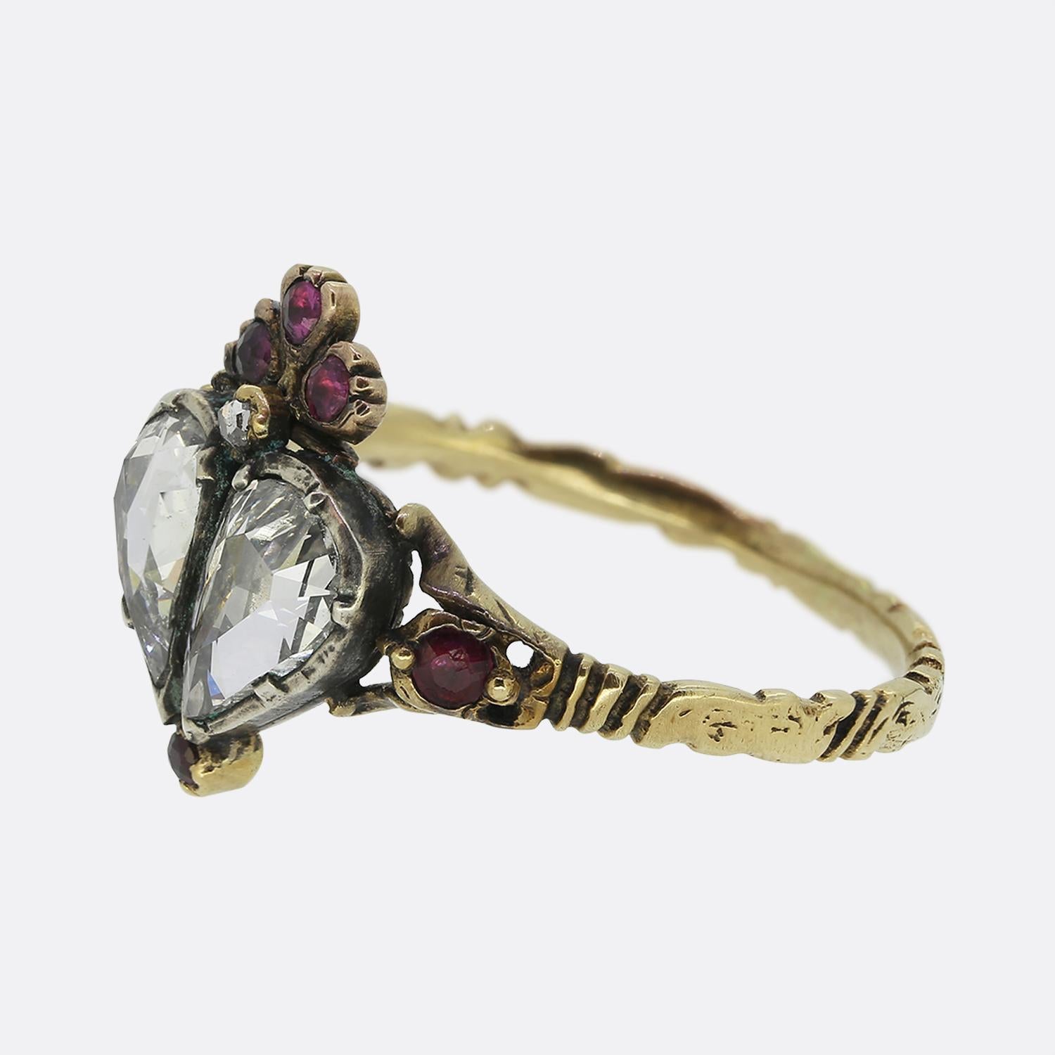 Aquí tenemos un precioso anillo victoriano de doble corazón. Esta romántica pieza presenta dos diamantes blancos talla rosa en forma de corazón en su centro. Este dúo focal está coronado por un trío de rubíes rojos y un diamante talla rosa. La
