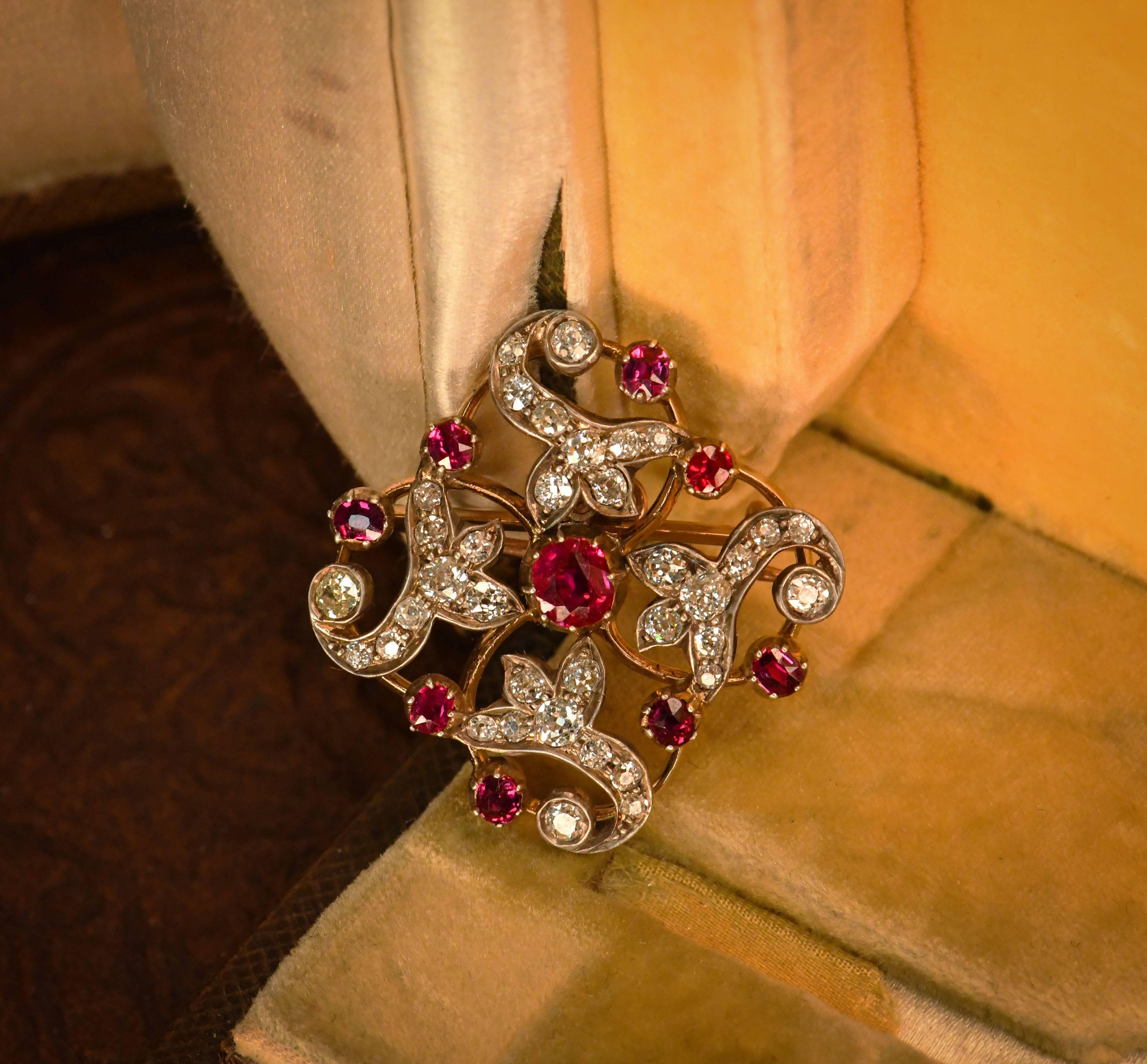 Graceful floral twirls of yellow gold framework enclosing bright and lively old European cut diamonds which twinkle and dance in the light. Enriching this elegant design are vivid rubies delicately placed around the diamonds. A larger ruby sits at