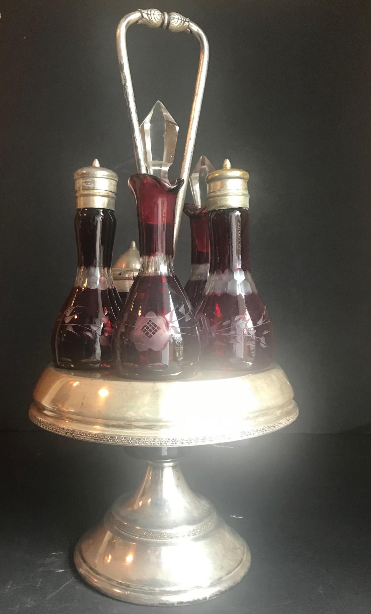 This charming Victorian silver plated cruet set was made by Reed & Barton. The set is marked pattern number 445 and features five Ruby Cut to Clear Bohemian Art Glass containers that sit upon a silver plated circular caddy. The garland etched caddy