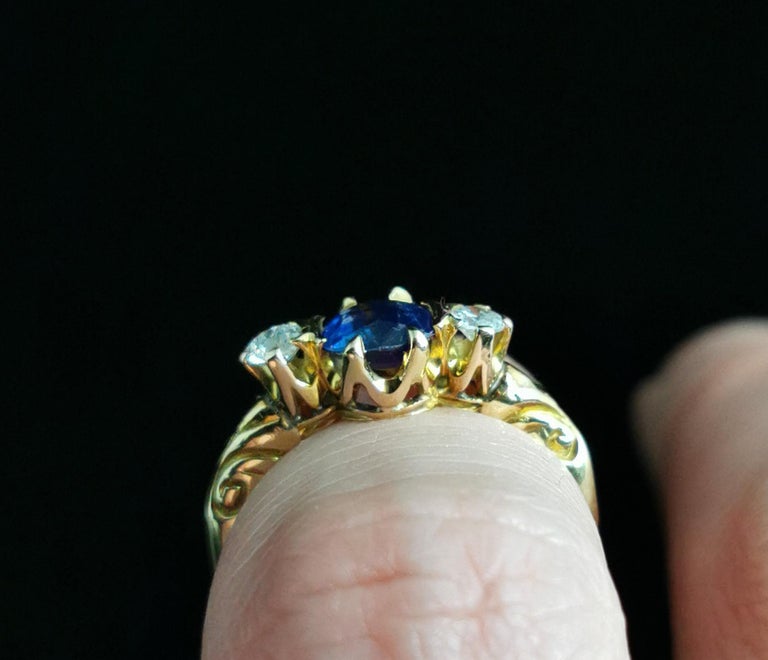 A stunning antique, Victorian era Sapphire and Diamond three stone ring.

The ring has a substantial 18ct yellow gold band, tapering from the deeply engraved and shaped shoulders.

The centre front features a beautiful rich and deep blue cushion cut