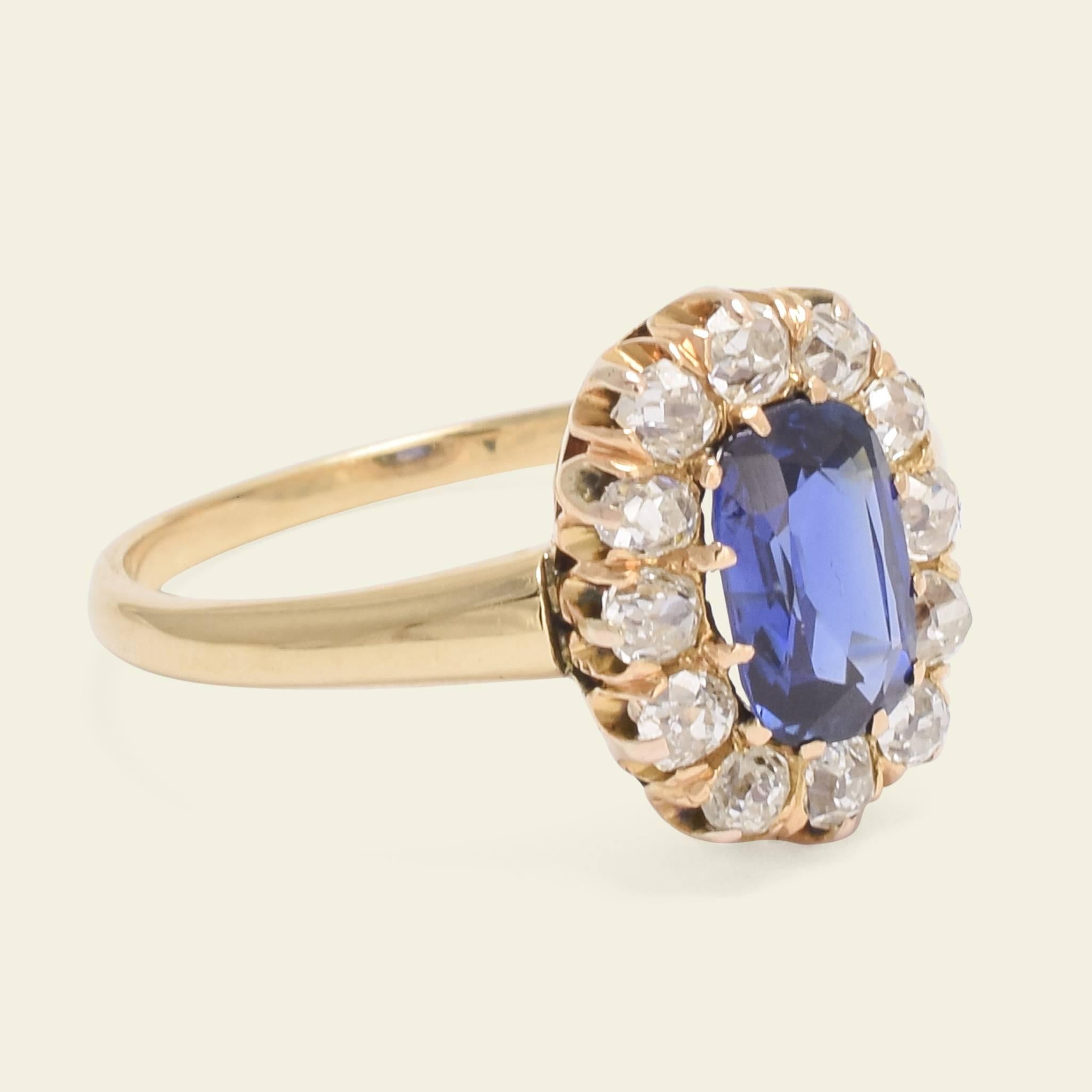 This beautifully proportioned late Victorian cluster ring is fashioned in 14k yellow gold with a 1ct cushion cut sapphire set within a halo of 12 approximately .04ct old mine cut diamonds. The vibrant blue gem is extra special not just for its lush