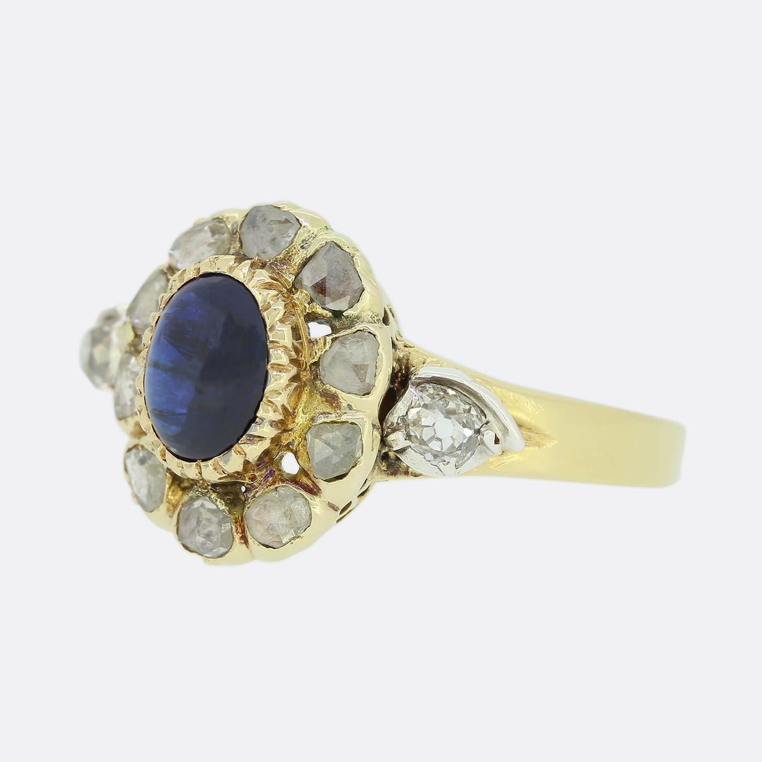 This is an 18ct yellow gold oval cluster ring. The ring is set with a centralised oval cut rub-over set cabochon sapphire which is surrounded by a cluster of rose cut diamonds. The head of the ring originally started life as a necklace clasp.
The