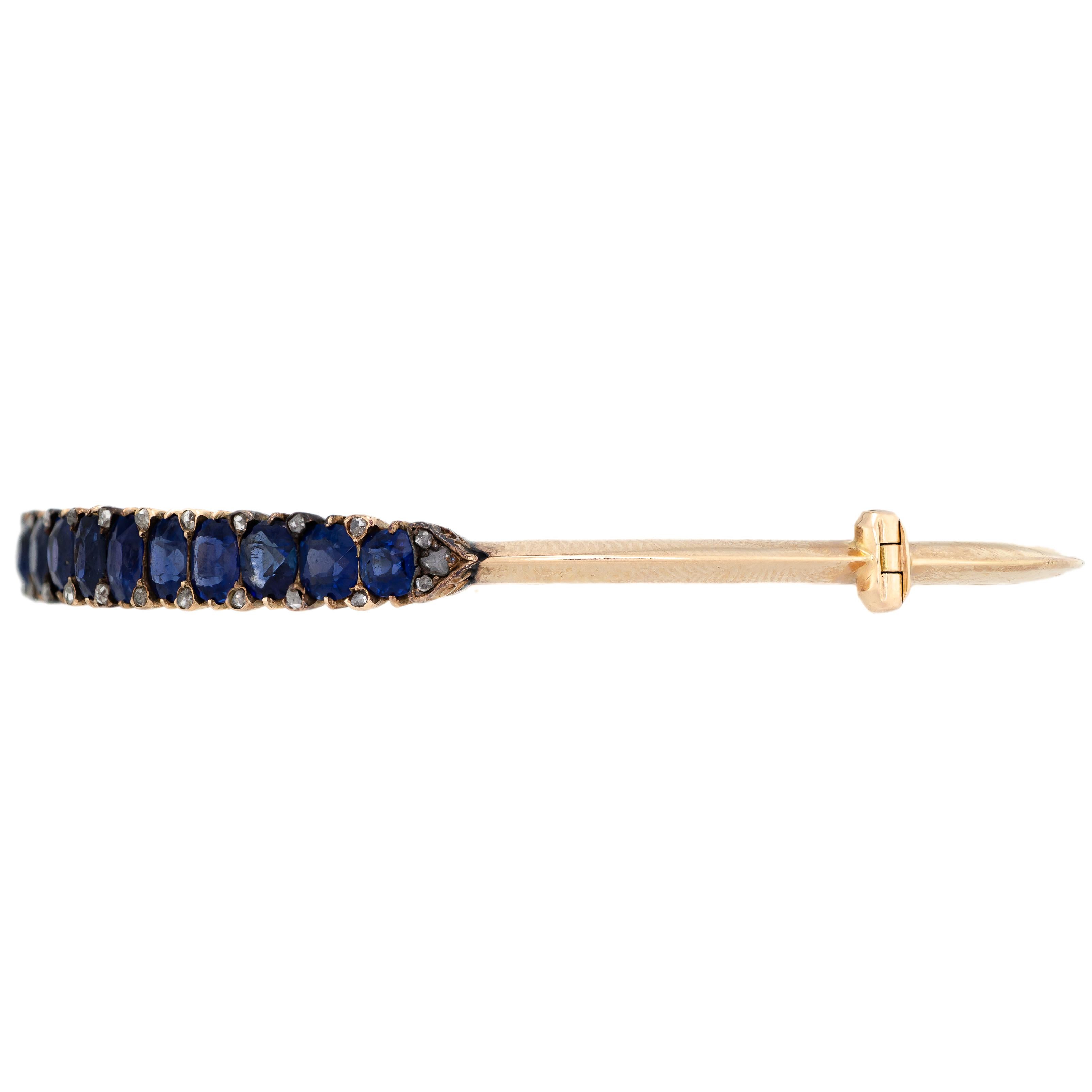 A stunning deep rich blue color graduated in size oval natural sapphire and rose-cut diamond. Crafted out of 15kt gold, this lovely knife-edge style hinged bangle bracelet is Victorian, dating Circa 1880. The top of this elegant Victorian bracelet