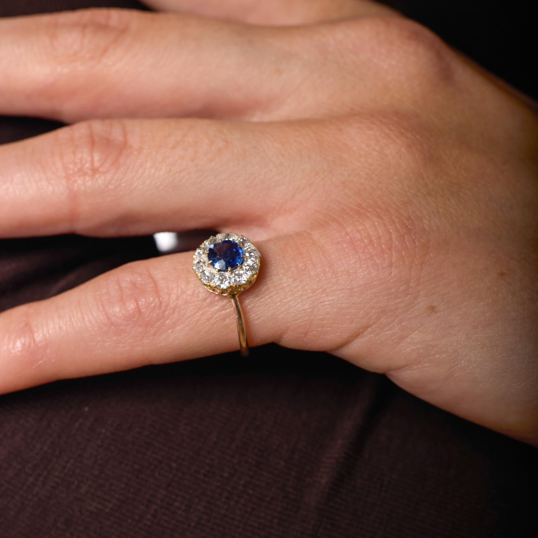 Cette bague victorienne à grappes présente un saphir bleu lumineux encadré par un cercle radieux de diamants taillés à l'ancienne, chaque pierre reflétant l'éclat doux et romantique caractéristique de l'artisanat du XIXe siècle. Le contraste entre