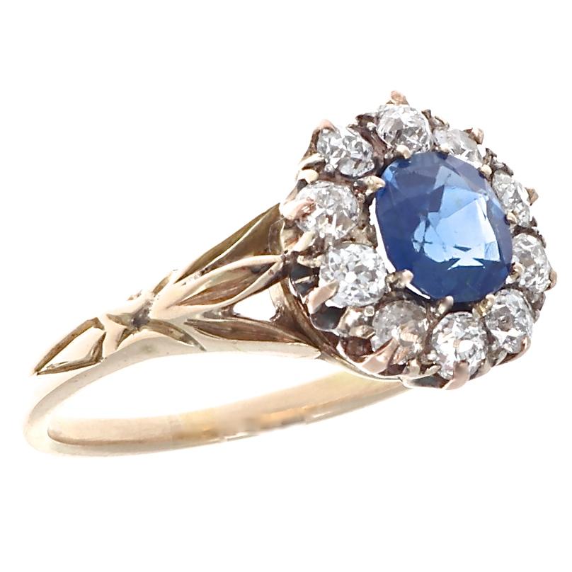 A beautiful blue faceted .75 carat blue sapphire, surrounded by 10 old European diamonds weighing approximately .50 carats, G-H color, SI clarity. Prong set in 18k with beautiful minimalistic carving on the band, this is Victorian high jewelry at