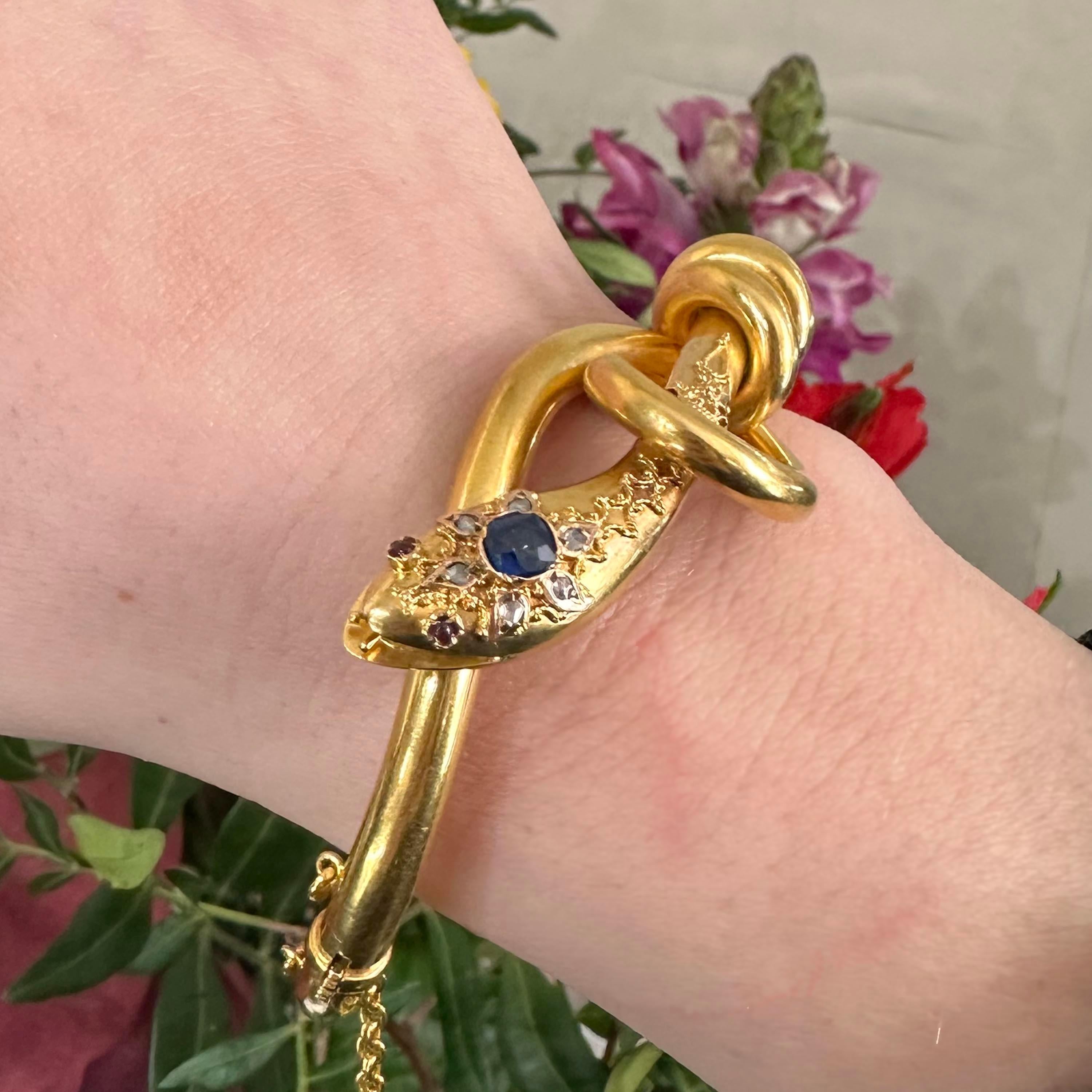 A Victorian snake bangle, with a cushion cut sapphire set in the head, with a surrounding cluster of rose cut diamonds, in pear shape settings and cabochon cut ruby eyes, with twisted wire and granulation decoration, with an open mouth featuring