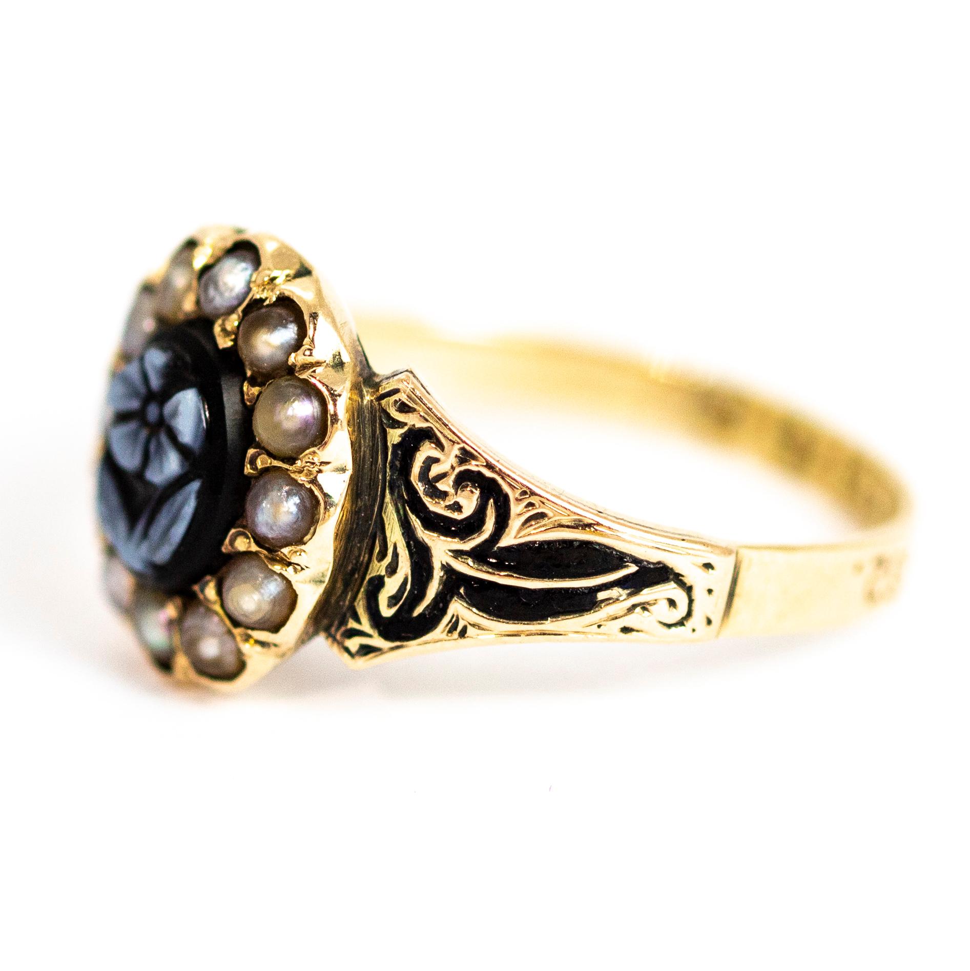 This ring is a wonderful example of a Victorian mourning ring. The 'forget me not' flower id intricately carved from a sardonyx stone. Around the carving sits a halo of delicate pearls and the shoulders of this ring feature enamel detail. The