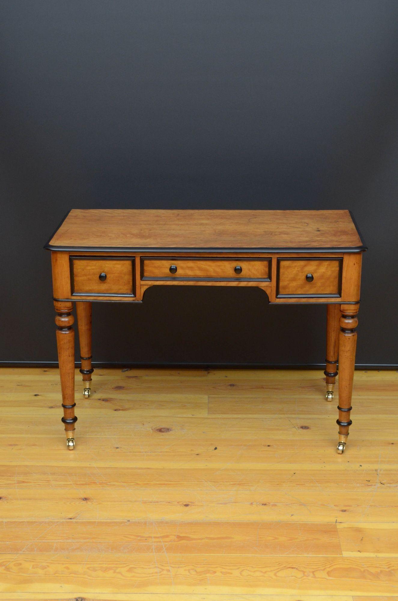 ST039 Attractive Victorian satin birch dressing table or writing table, having oversailing top with ebonised edge and three frieze drawers with ebonised turned knobs, all standing on turned tapered legs terminating in original brass castors. This