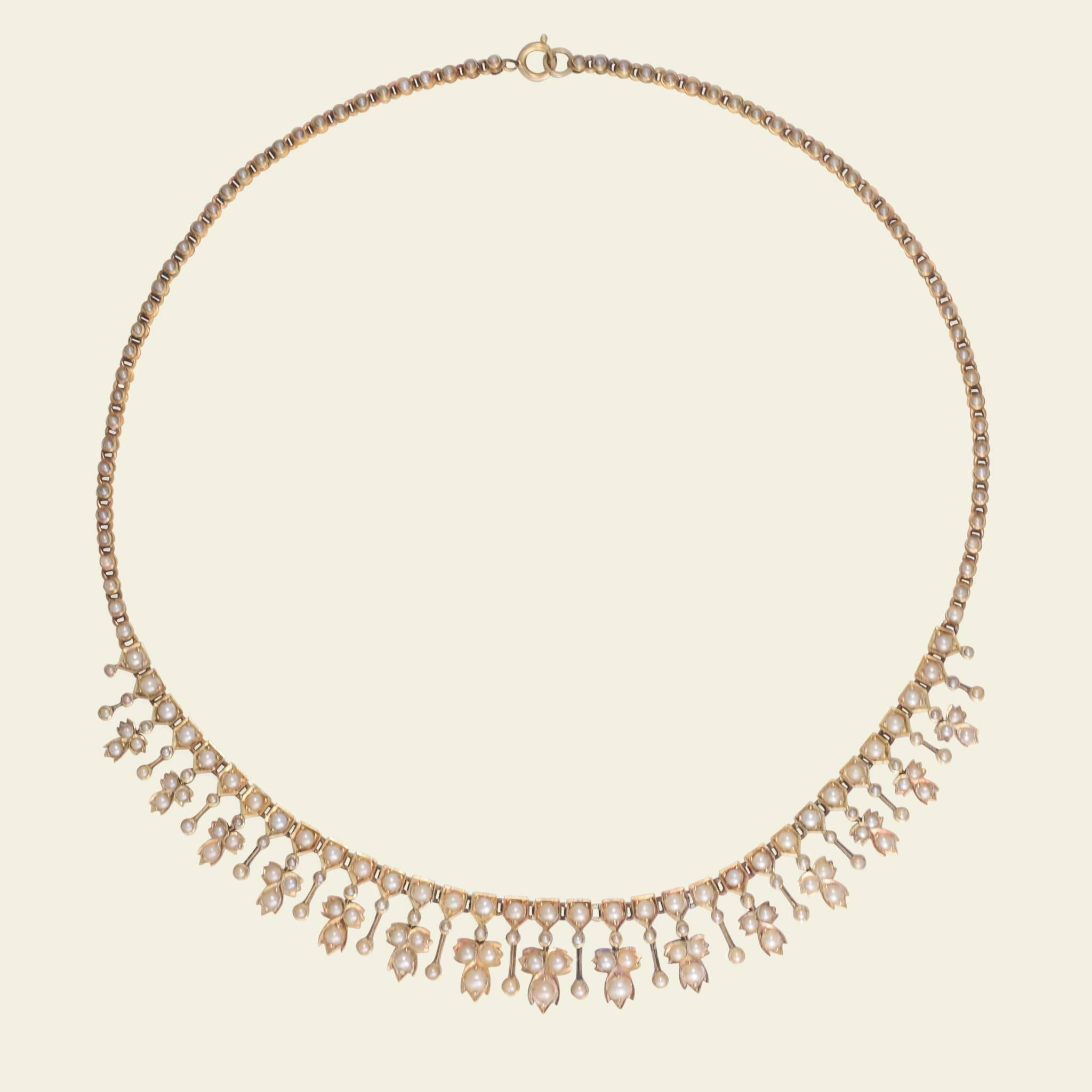 This mid Victorian fringe necklace is fashioned in 18k gold and almost glows with the rich luster of seed pearls. The drops that form the fringe alternate between simple pearl-studded bars and more elaborate floral-themed trefoil elements. Even the