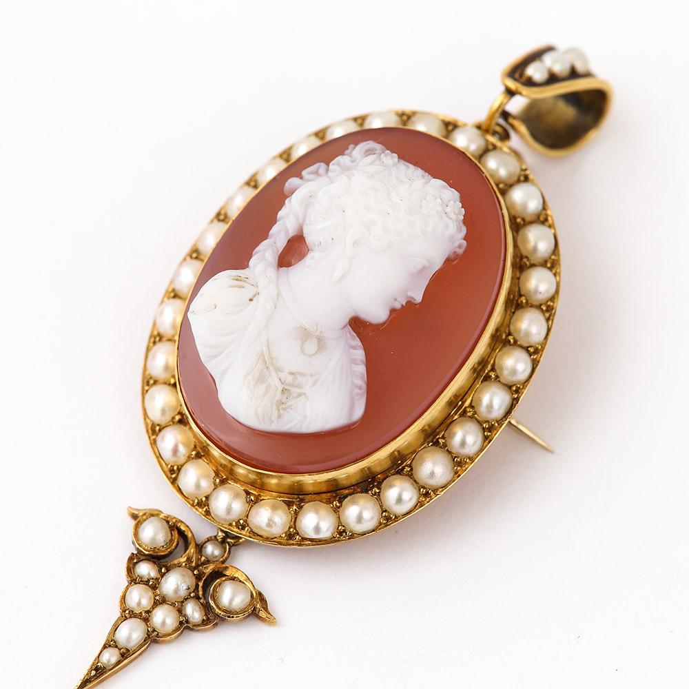 A lovely Victorian shell cameo and pearl pendant and brooch surmounted with pearls displaying a fine carving of a lady in the Greco-Roman style wearing drop earrings and a pendant around her neck. The gold mount is unmarked but tested as 15 karat