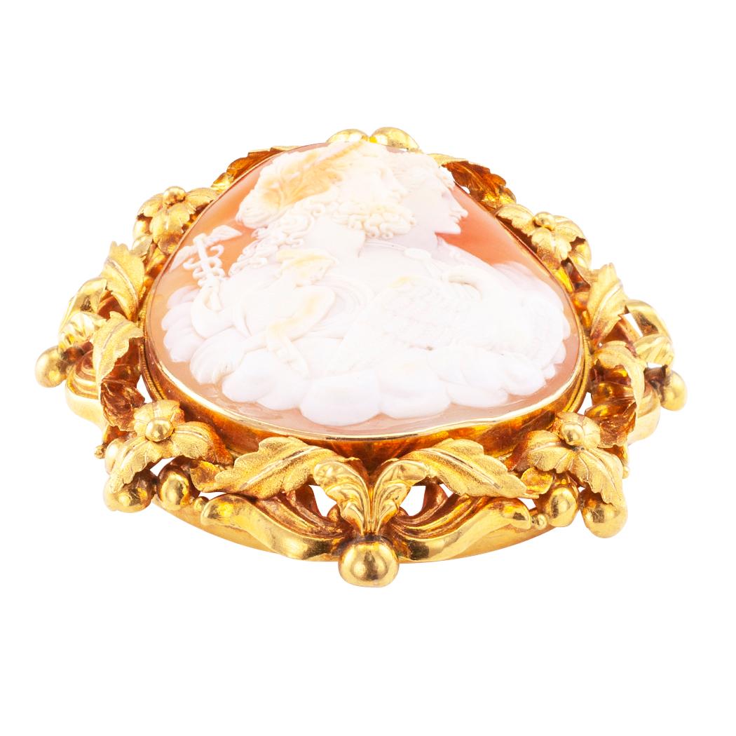 Victorian shell and gold cameo brooch circa 1890. The oval shell carving depicting four mythological deities, bezel-set within a wide and elaborate 18-karat yellow gold frame comprising various foliar motifs. When we first saw this cameo, we