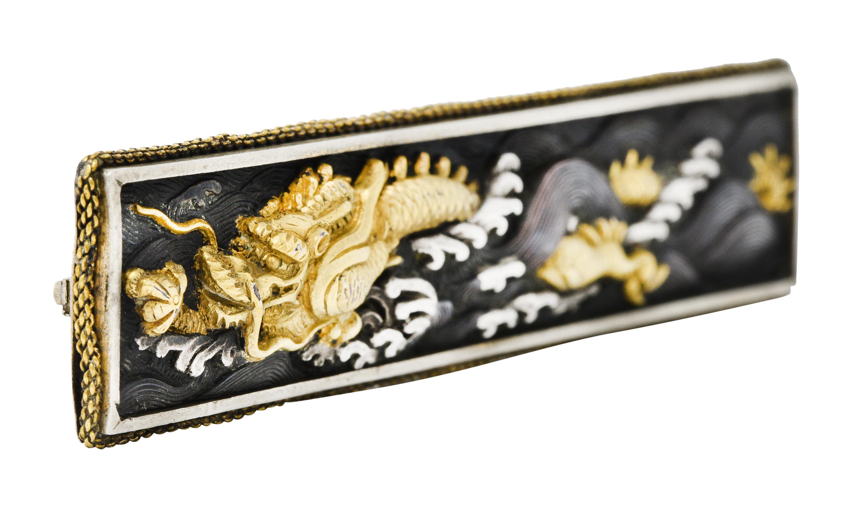 Rectangular bar brooch centers a shakudō tablet darkened with patina and accented by silver and 18 karat gold appliqué

Depicting the serpent dragon king Ryujin clutching a talisman that controls the swelling and stylized tides

With a silver border