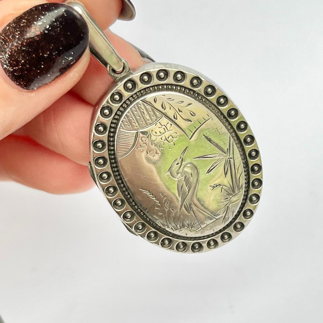 On one side of this beautiful locket there is engraving of a heron with a beautifully ornate frame surrounding it. The other side of this locket is decorative and finely engraved. 

Dimensions: 37x30mm

Weight: 10.1g