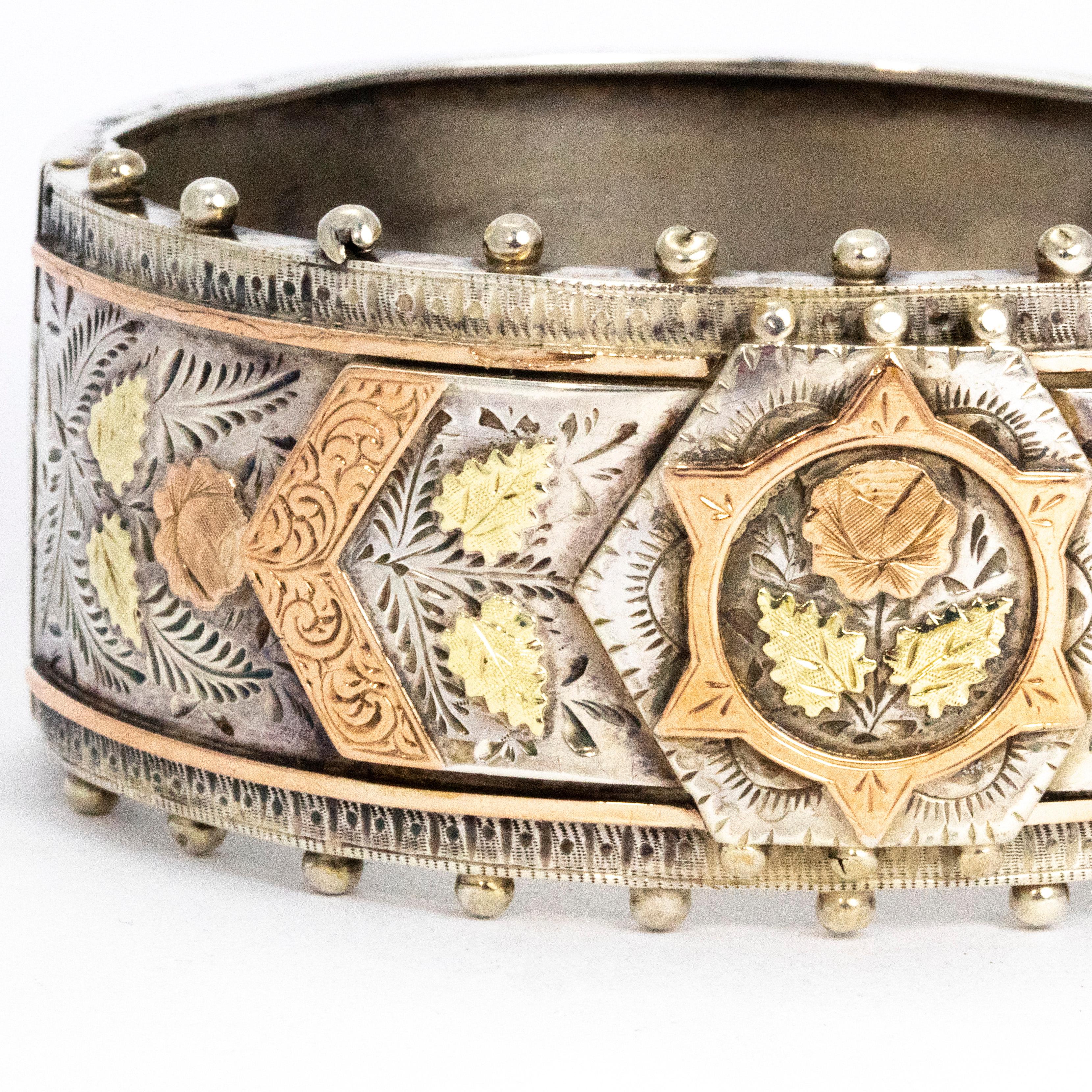 This stunning bangle features silver, yellow gold and rose gold details. The main band is modelled in silver and also has silver plaque overlays. The main plaque has a gorgeous flower priced together with yellow gold and rose gold and wither side of