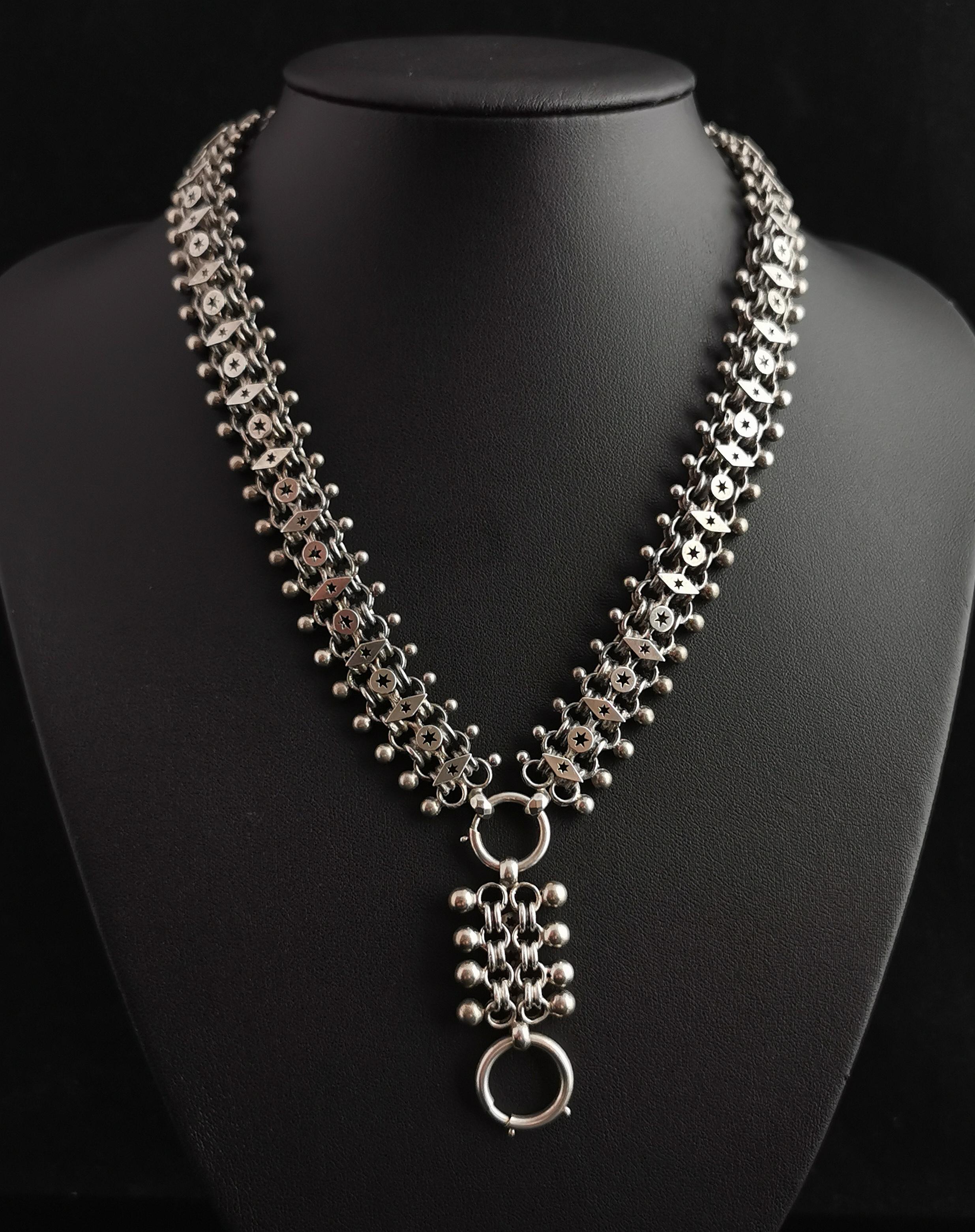 A beautiful antique, Victorian, Aesthetic era book chain necklace.

This is a day to night necklace with one side having an elaborate design of diamond and circular shapes each punched with tiny stars, this is the night side, when a little extra