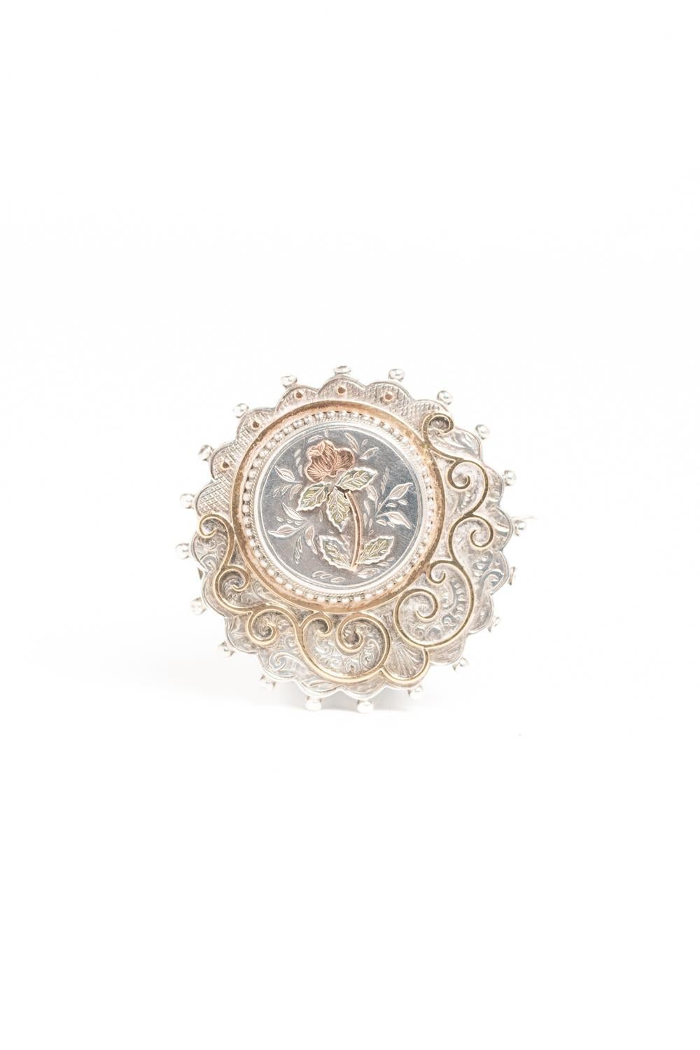 A beautiful Victorian silver brooch made circa 1880. It's typical of the late Victorian style with engraved stylized floral and geometric motifs around the edge with bobbles then a stunning circular band of gold around the brooch. In the centre is a