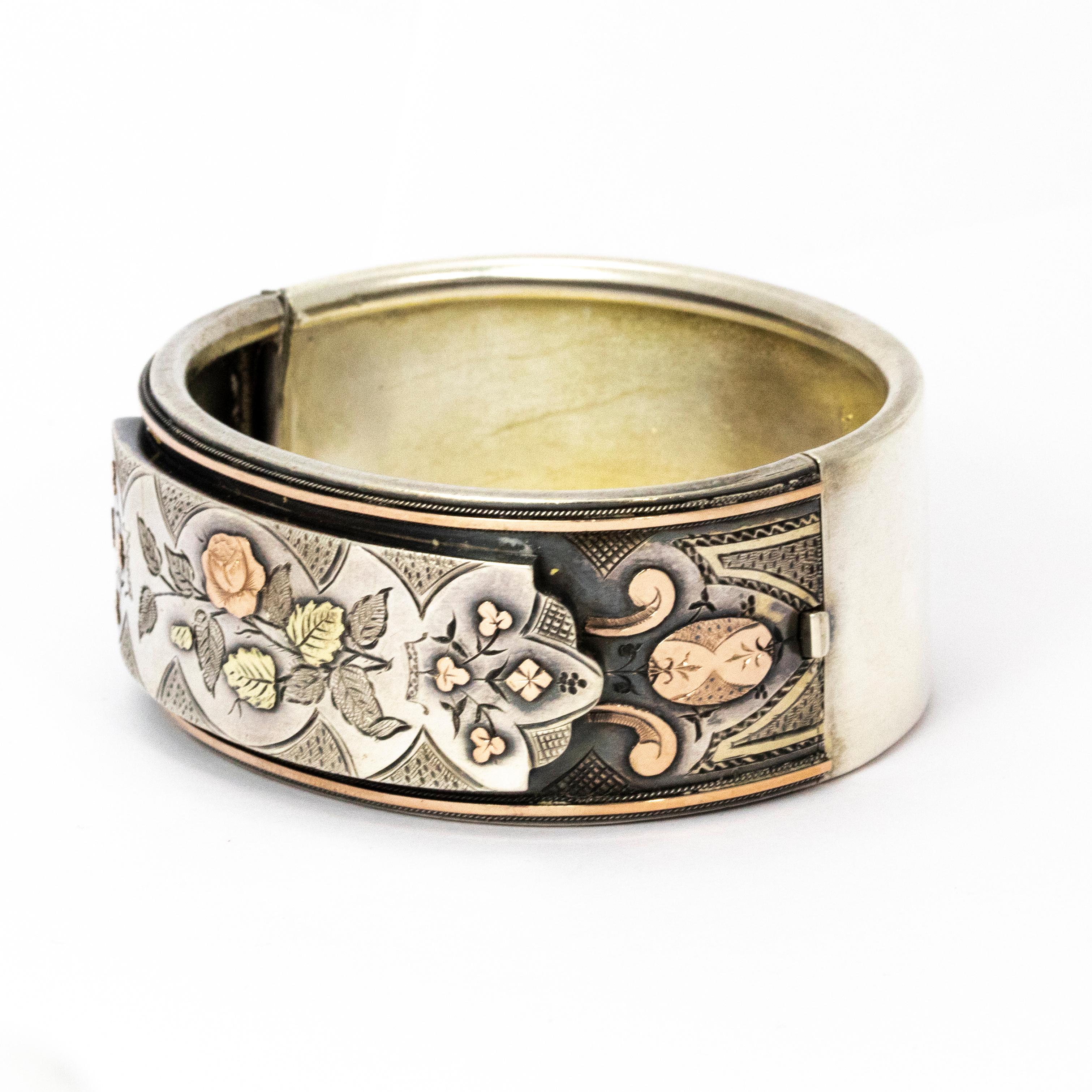 A brilliant antique Victorian bangle. It is meticulously engraved with a foliate scene of leaves and flowers, parts of the design are finely set with two tones of gold overlay. Modelled in silver.

Diameter: 6.2cm (from hinge to clasp)
Height: 2.5cm