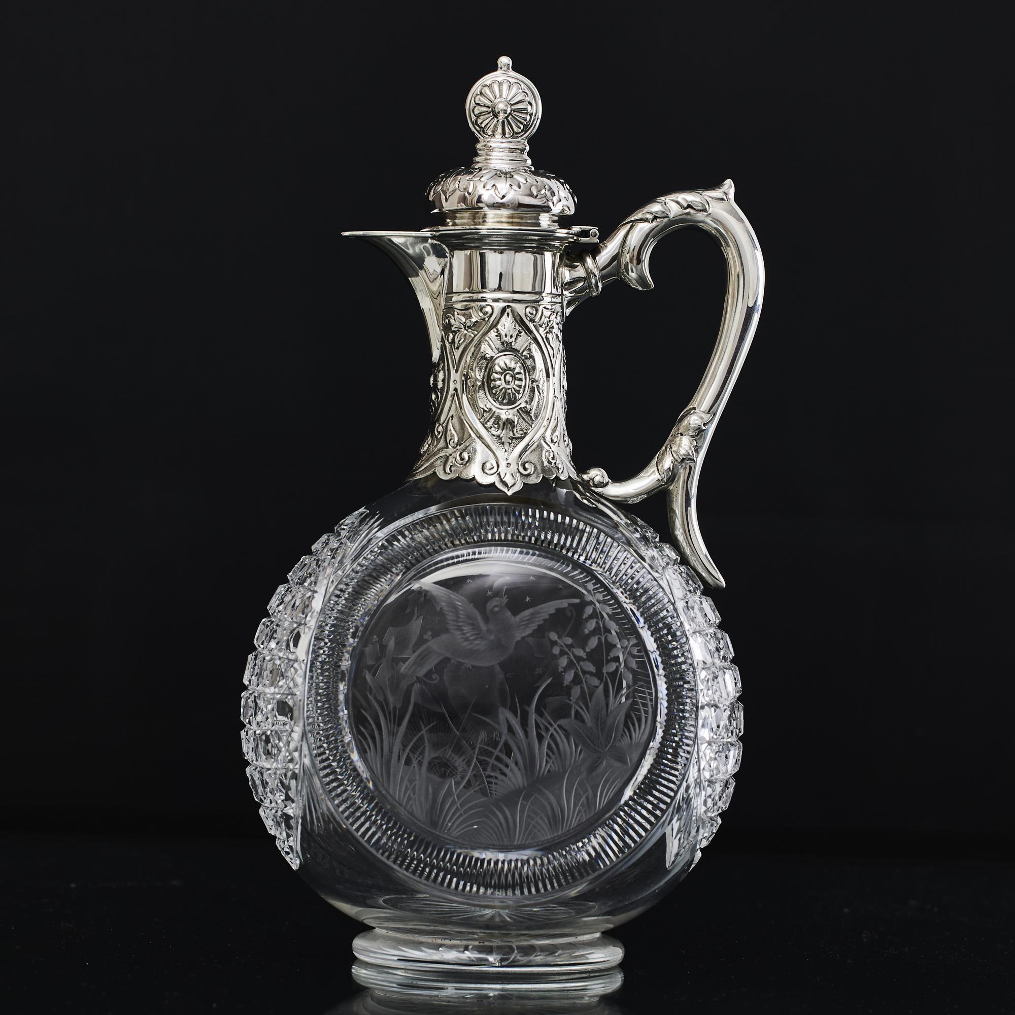Beautiful, late-Victorian, antique cut glass wine jug with hand chased silver cover and mounts. The glass body is skilfully decorated with hand engraved panels incorporating an owl and a flying dove against a countryside setting. The glass body