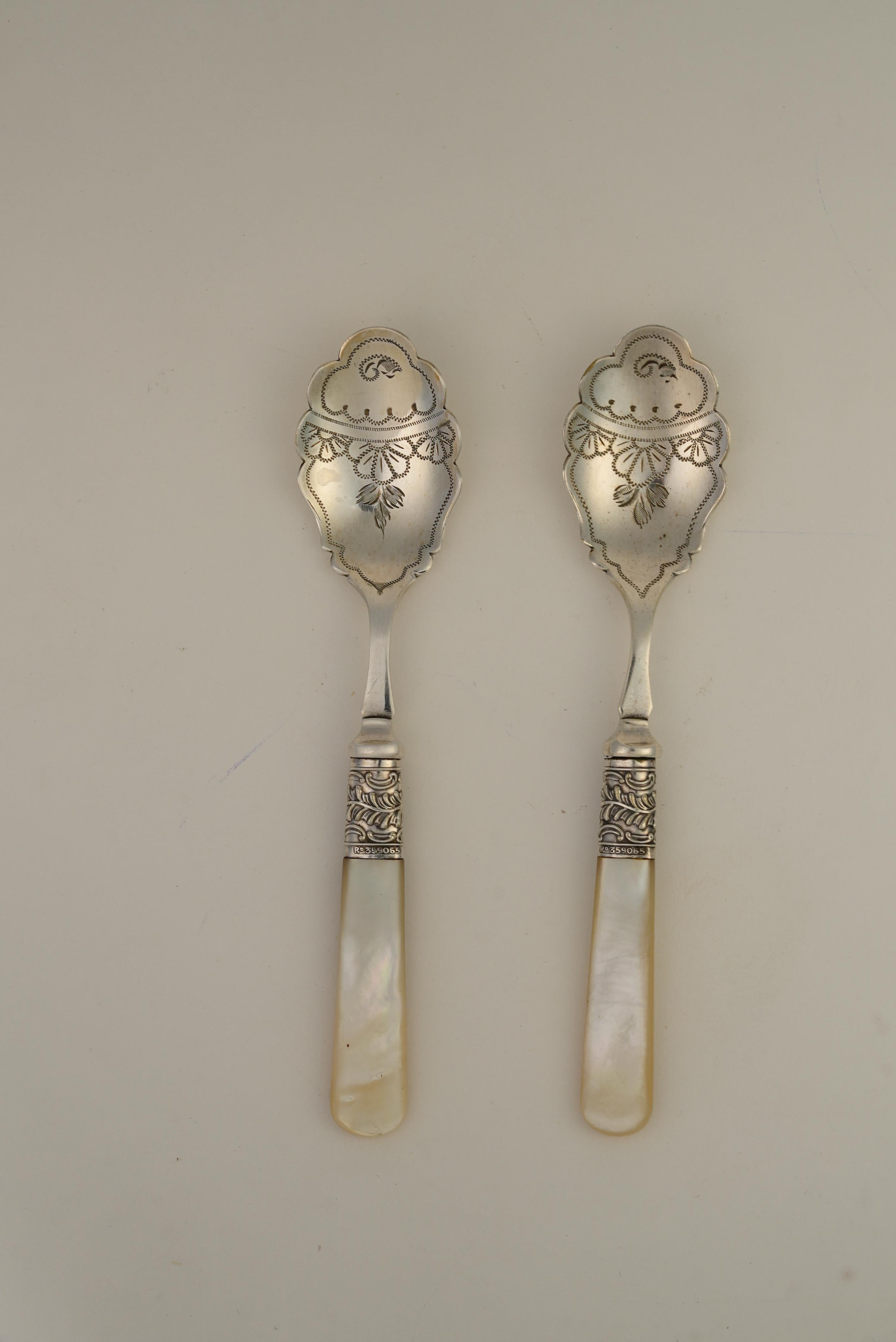 A refined pair of late Victorian silver-plated spoons with scalloped, engraved bowls and luminous mother-of-pearl handles, accented by ornate silver ferrules. Housed in their original fitted case with velvet and silk lining, this c.1890s English set