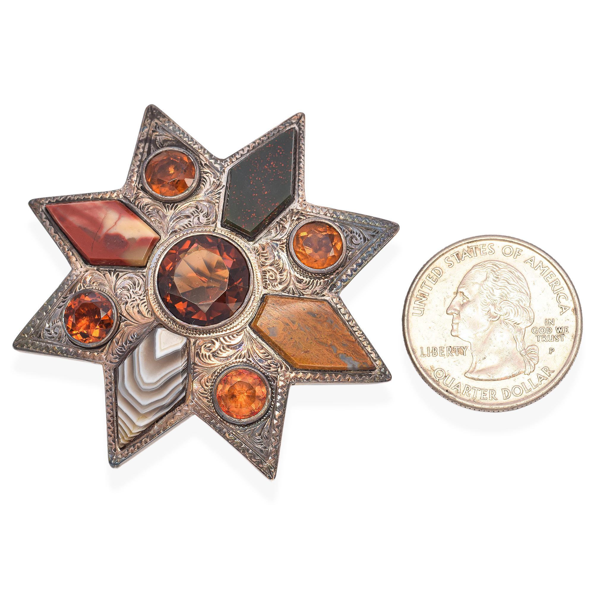 A striking brooch designed in a star motif. It features a central large round citrine gemstone, surrounded by various geometric stones in warm hues, all set in intricately engraved metal. The piece showcases a harmonious blend of colors and shapes,