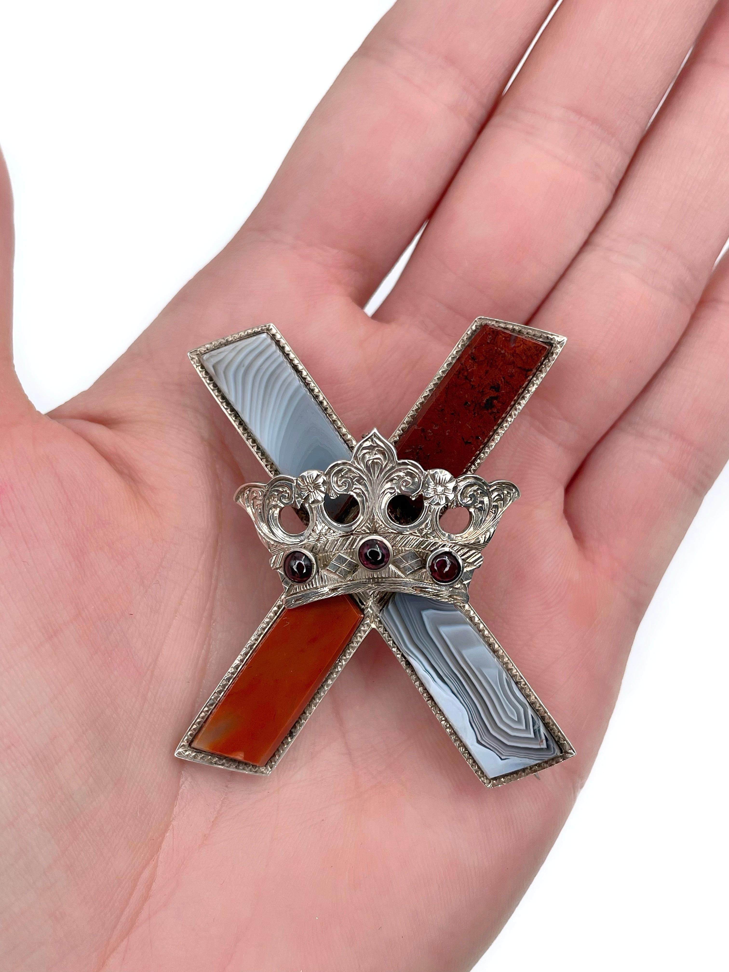 This is a Victorian era Saltire cross and crown pin brooch crafted in silver. Circa 1880. 

It features Scottish agates and garnets.  

Saltire, also called St. Andrew’s, cross is a heraldic symbol in the form of a diagonal cross. In the 16th