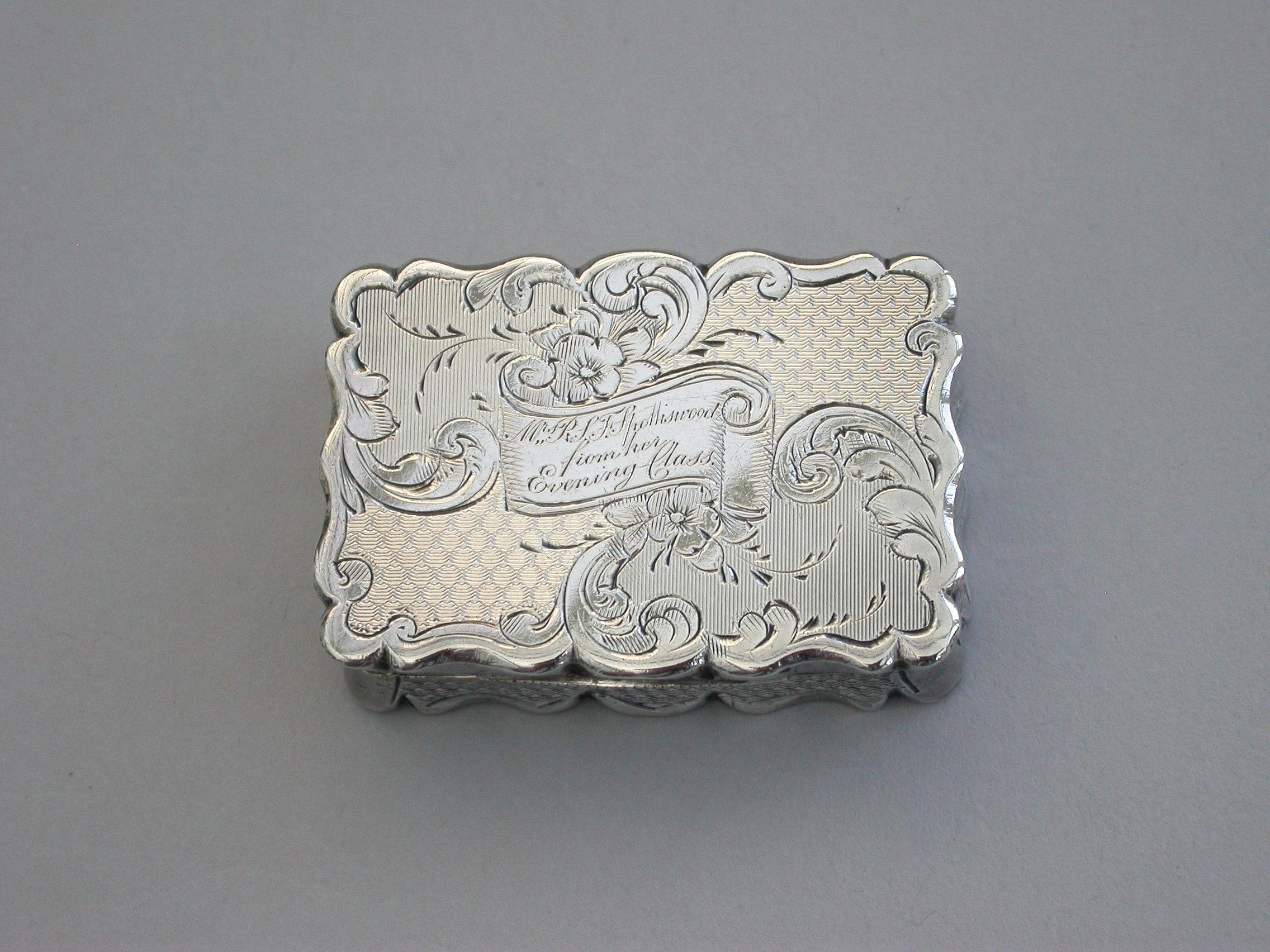 A charming and fine quality Victorian silver Vinaigrette of rectangular form with scalloped edges and all-over decoration of engine turned panels separated by engraved scrolls and flowers. The cover with central cartouche formed as an open scroll