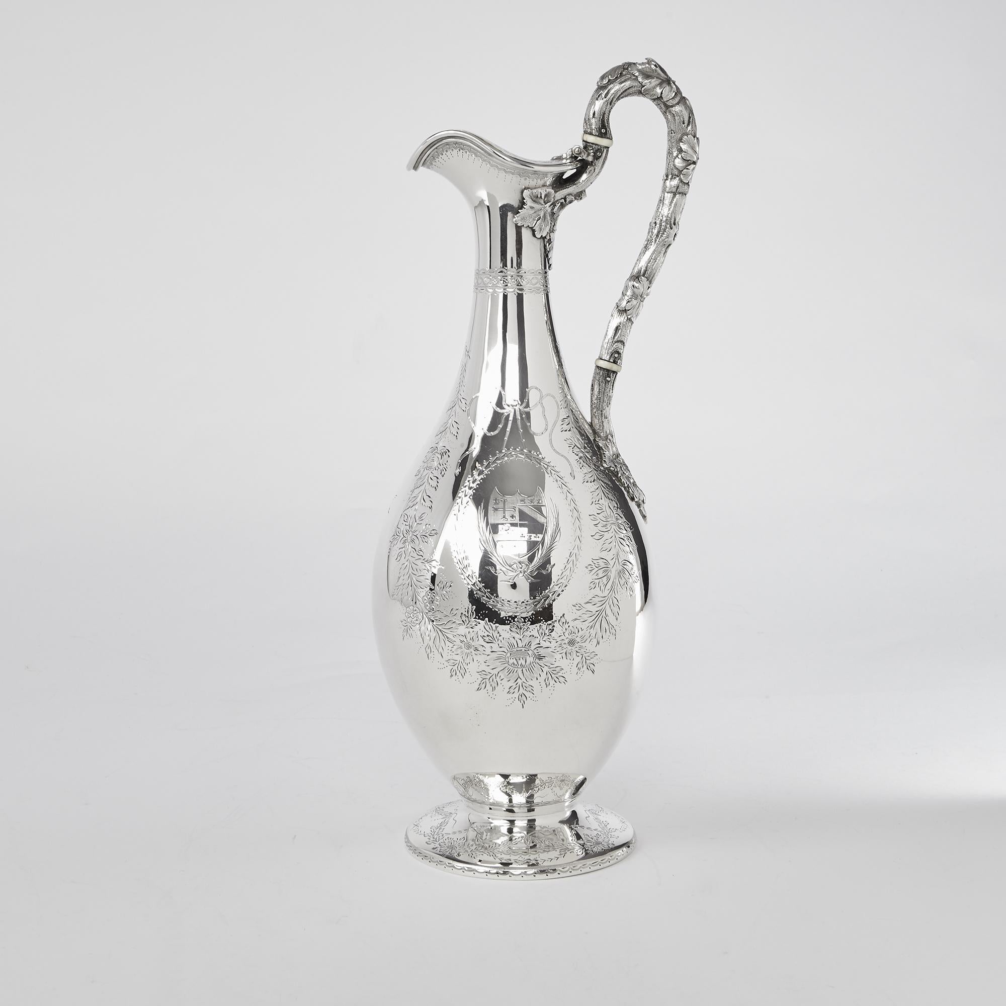 An extremely elegant Victorian silver claret jug with pear-shaped body decorated with hand-engraved floral swags and garlands. It has an oval cartouche on either side containing family arms and a banner on one side engraved 