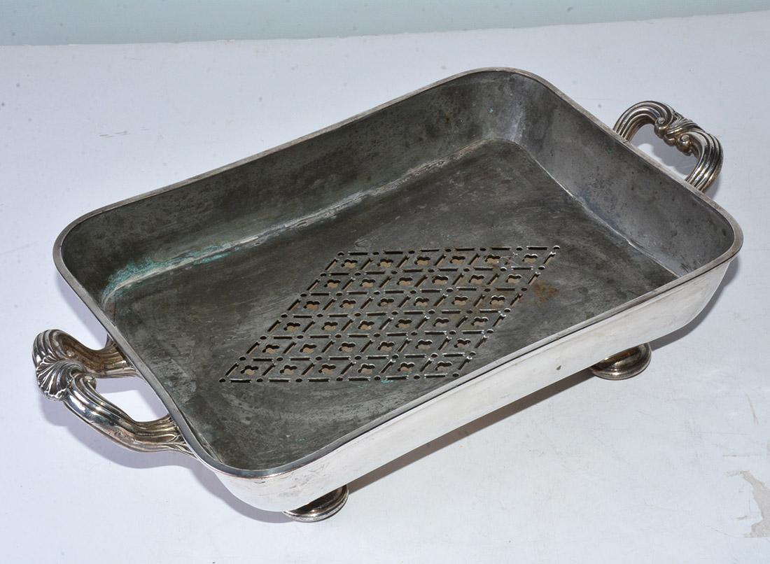 The Victorian silver plated and footed serving dish has space below the metal grill for holding hot water to keep food warm for a longer period of time. The metal would also retain heat. One corner of the inner part of the dish has an opening for
