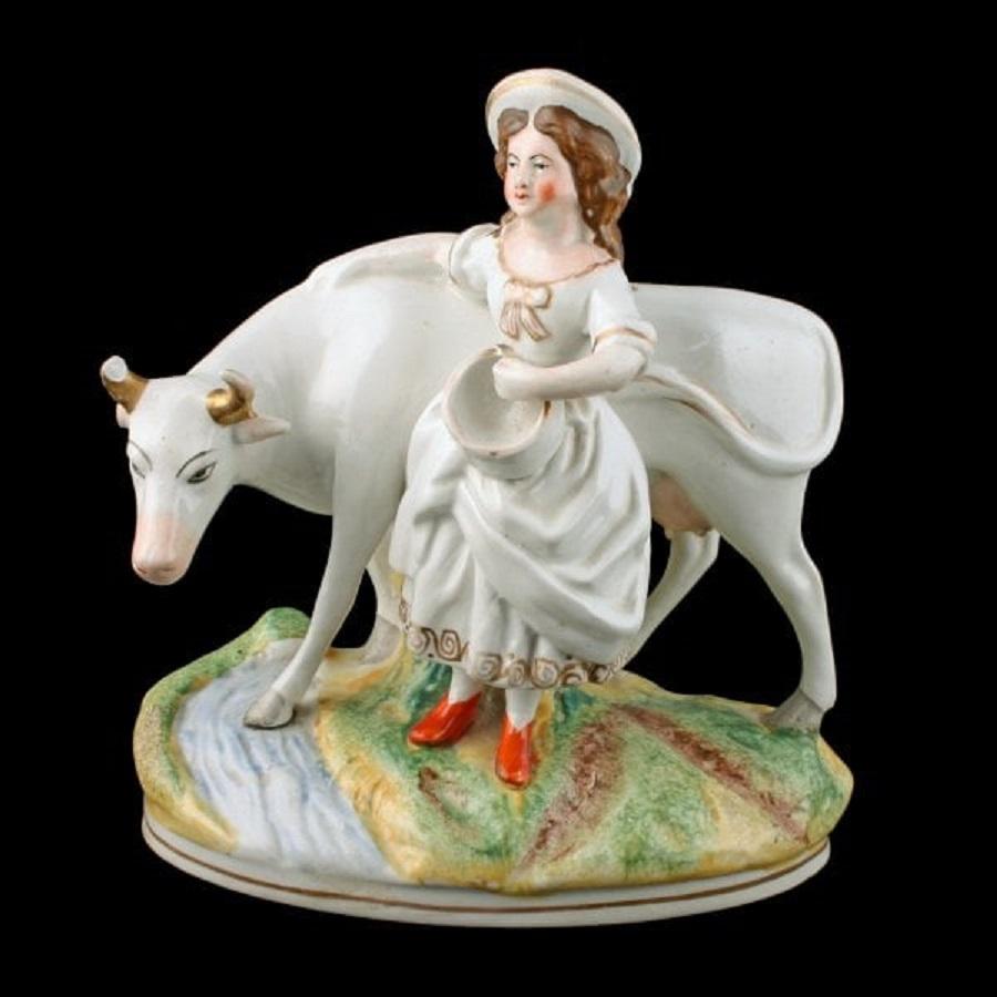 A middle of the 19th century Victorian Staffordshire pottery figure of a cow & milk maid.

The figures stand on an oval plinth base that is decorated as a field and stream with a gold line around the lower edge.

The milk maid is holding a milk