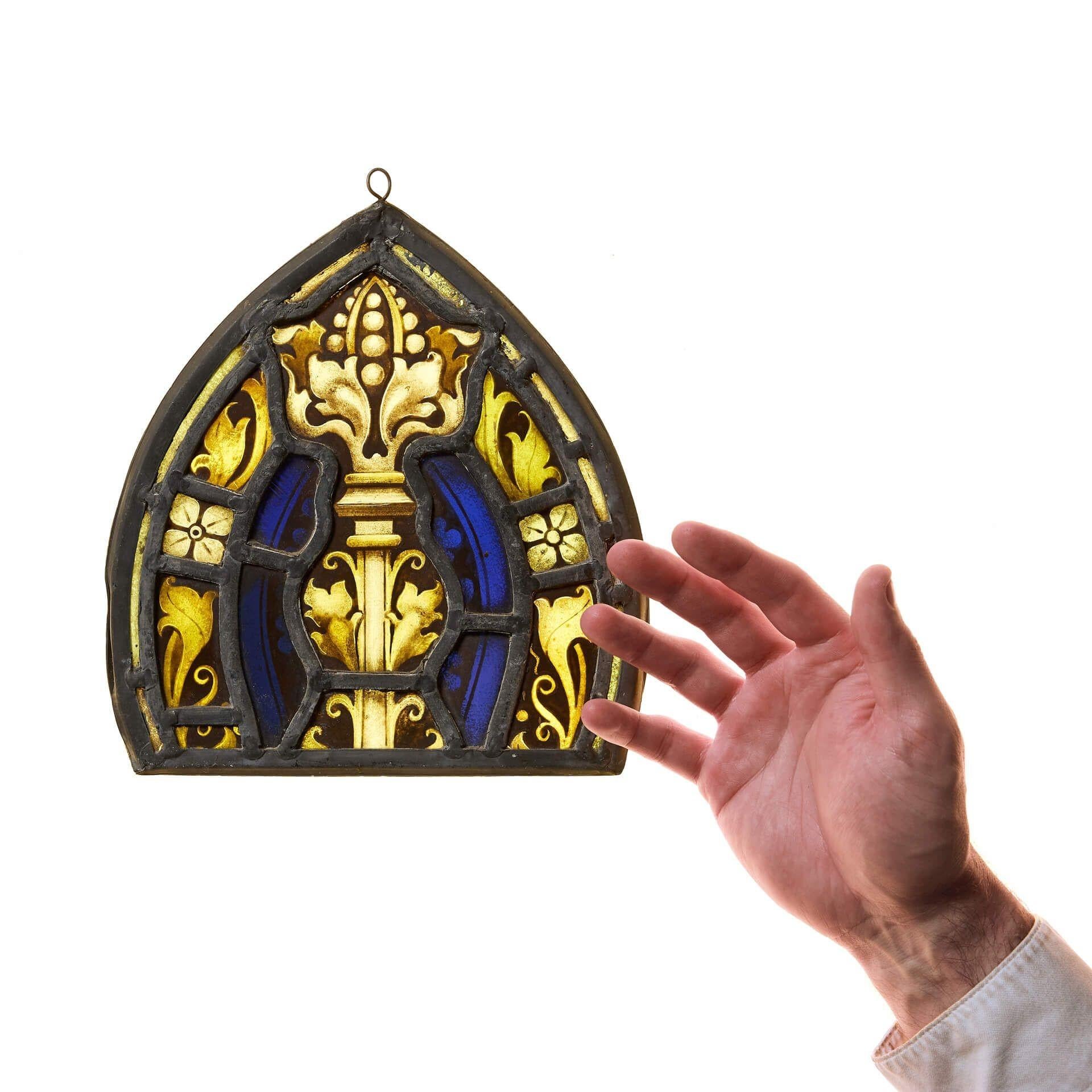 Petite suspension de vitrail de l'époque victorienne, vers 1890. Muni d'un cerceau au sommet, ce panneau de vitrail a une touche ecclésiastique avec son verre bleu et ses fleurs dorées peintes à la main. Accrochez-le à une fenêtre ou devant une