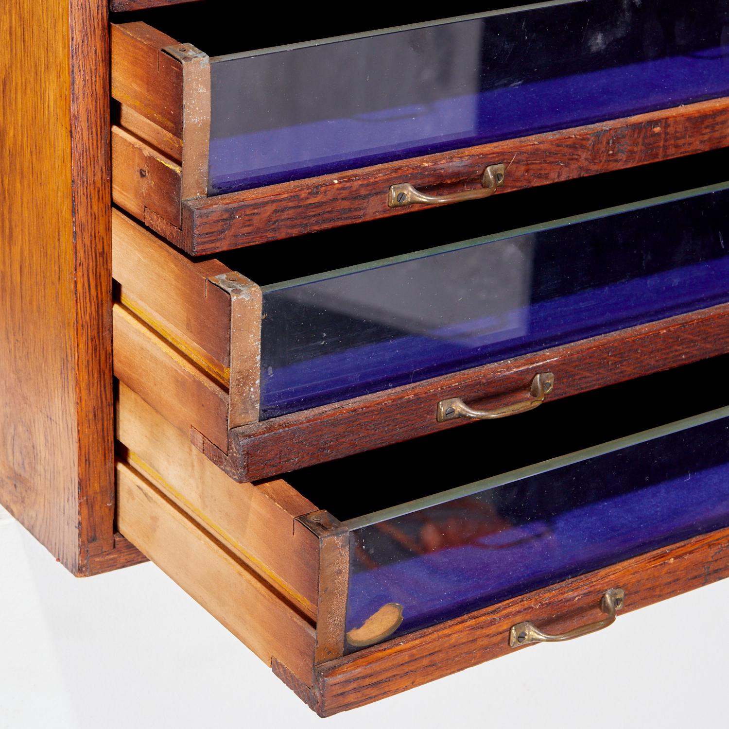 A rare and charming late 19th-century Star Threads spool cabinet, crafted in solid oak with five glass-fronted drawers and original brass pulls. This compact yet visually striking piece was originally used as a countertop display for sewing thread