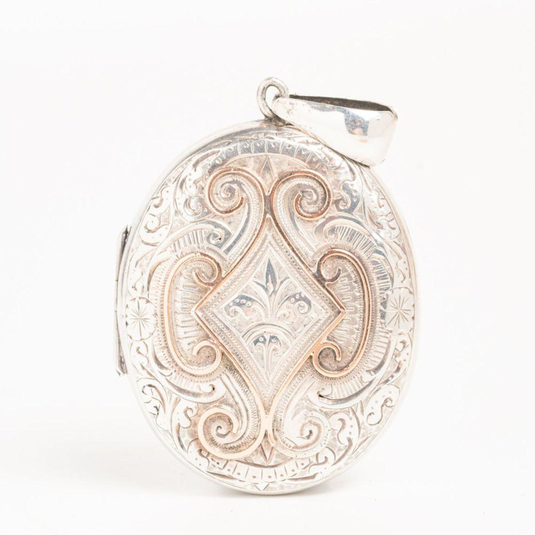 A charming antique Victorian Sterling silver and 9ct gold locket made in Birmingham in 1887 by Adie & Lovekin. The front of the locket is made in sterling silver and gold with a geometric, scrolled decoration with floral motifs surrounded the