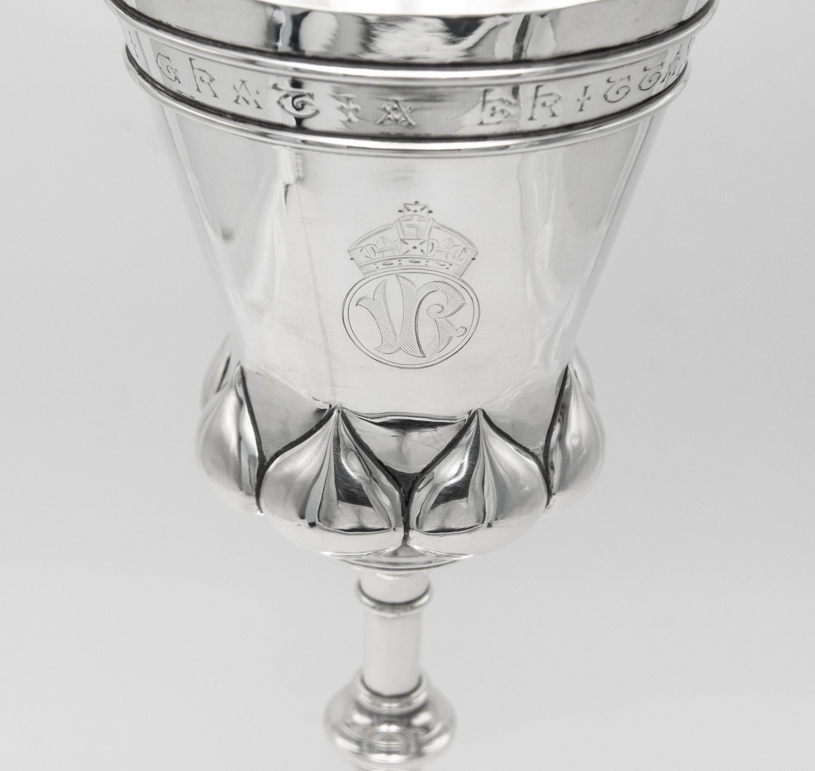 A Victorian Arts & Crafts period sterling silver chalice by Elkington & Co. Hallmarked for Birmingham 1890. 

The upper band of the tapering bowl with gothic style inscription 'VICTORIA DEI GRATIA BRITTANNIA REGINA F.D. 1890'. Below to one side is