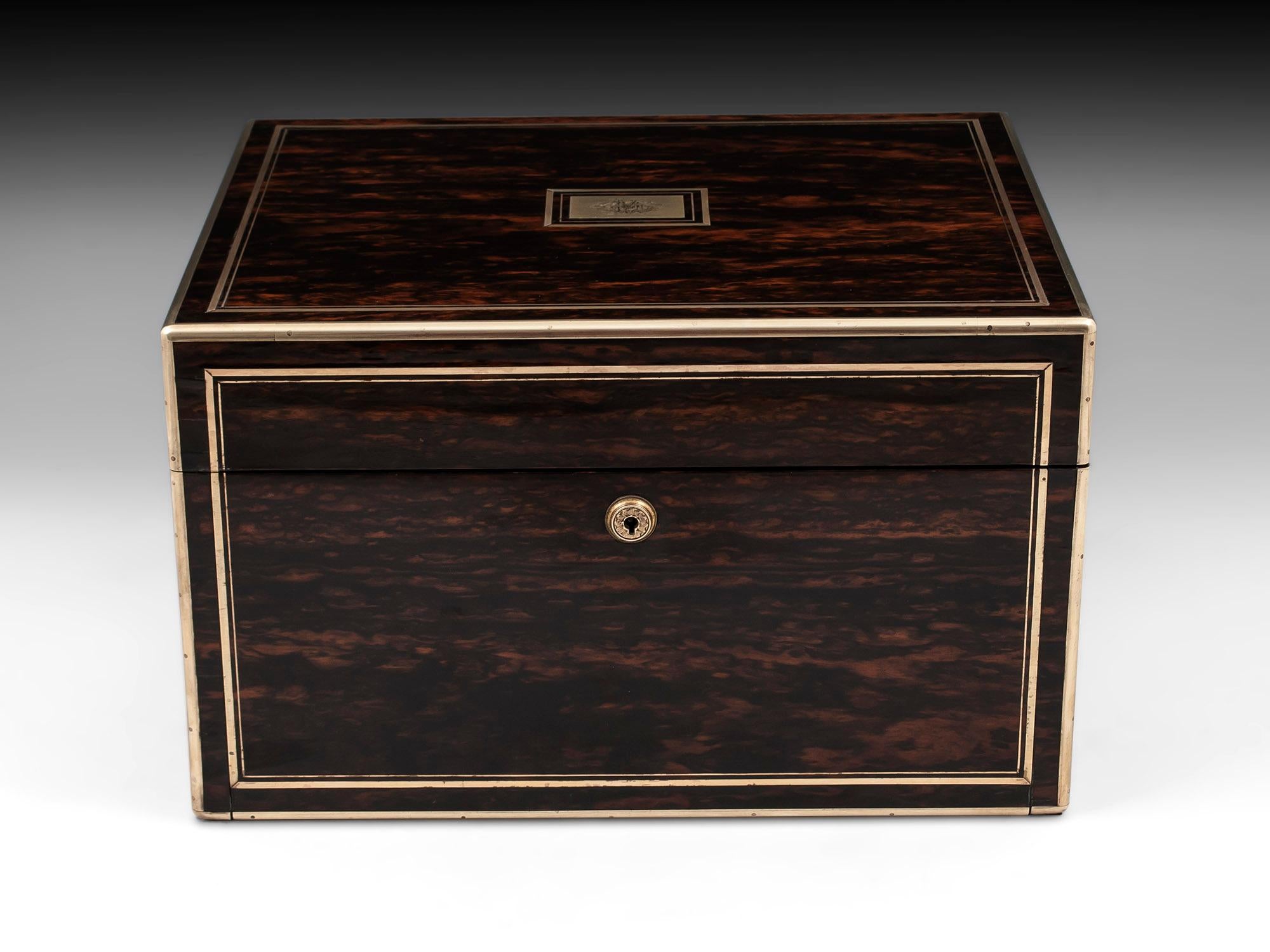 Sterling Silver Vanity box veneered in stunning coromandel, bound and double strung in brass, with robust campaign carry-handles and engraved escutcheon. The interior features twelve hobnail-cut glass containers with elaborately engraved silver lids