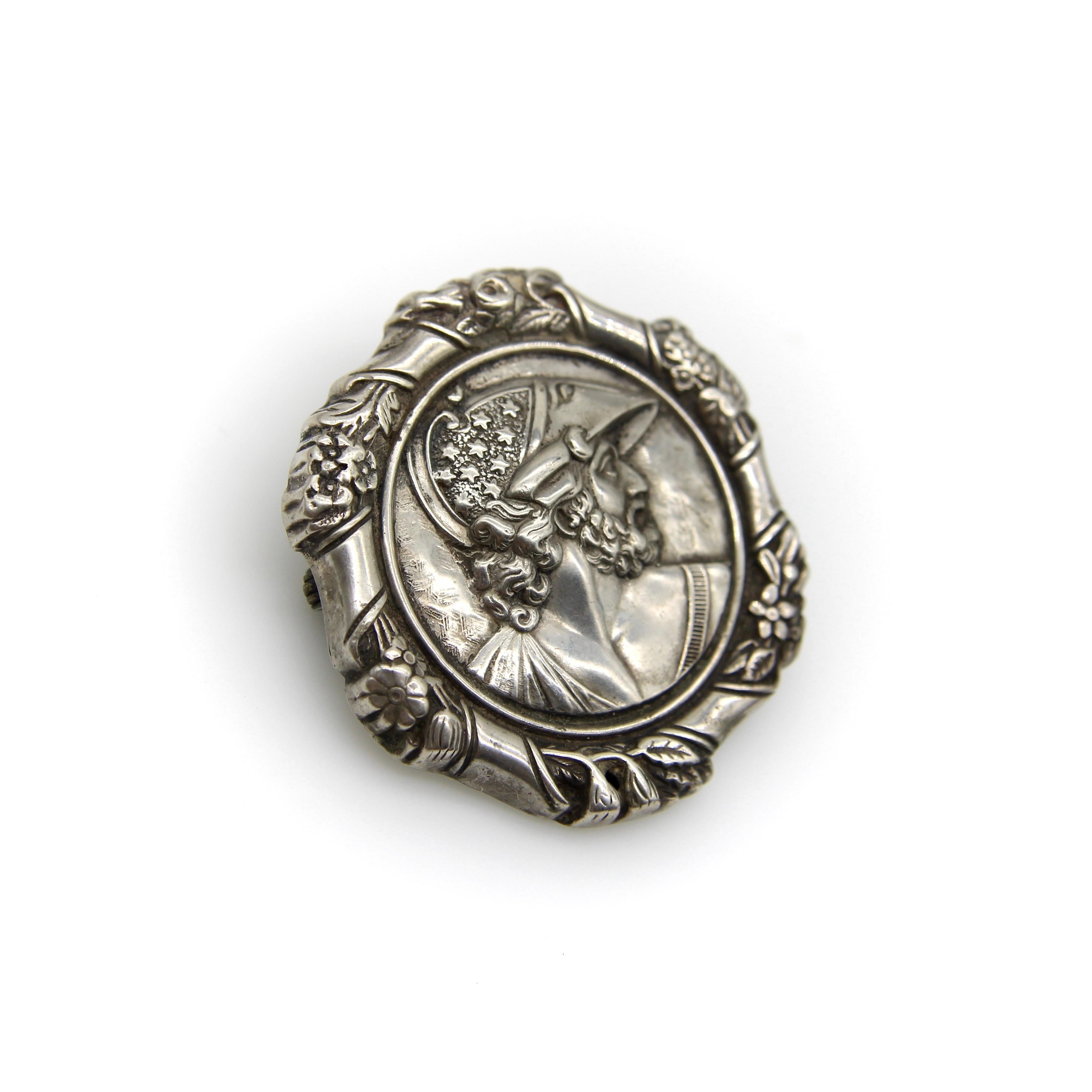 El llamativo perfil de un hombre barbudo, enmarcado por un estandarte de flores, es el punto focal de este broche de plata de ley de la época victoriana. El hombre del retrato parece un dios griego, con rasgos fuertes y masculinos, casco estrellado