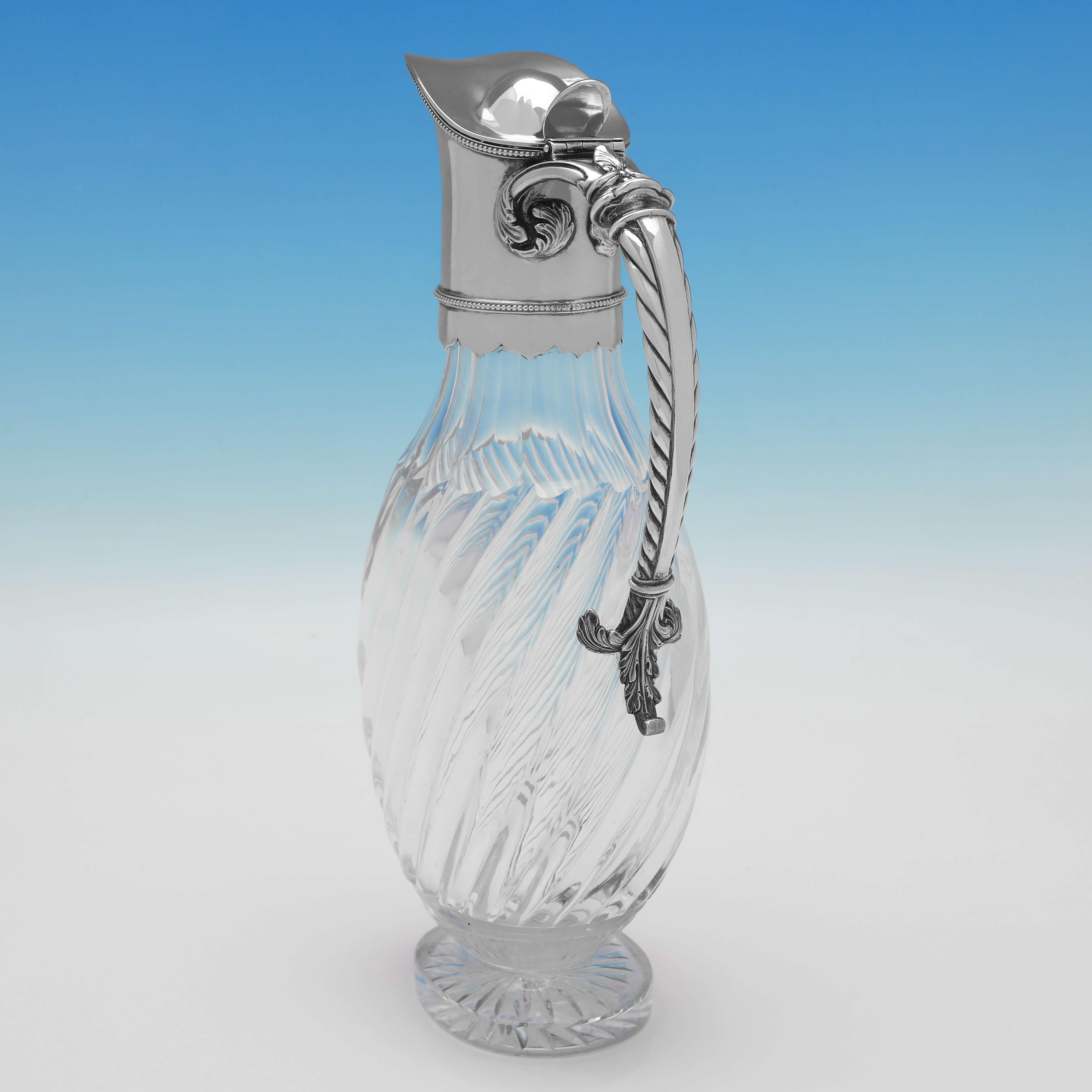 Hallmarked in London in 1886 by Edgar Finley & Hugh Taylor, this attractive, Victorian, Antique Sterling Silver Claret Jug, features a glass body with swirled fluting, a plain silver mount and a twisted silver handle. 

The claret jug measures