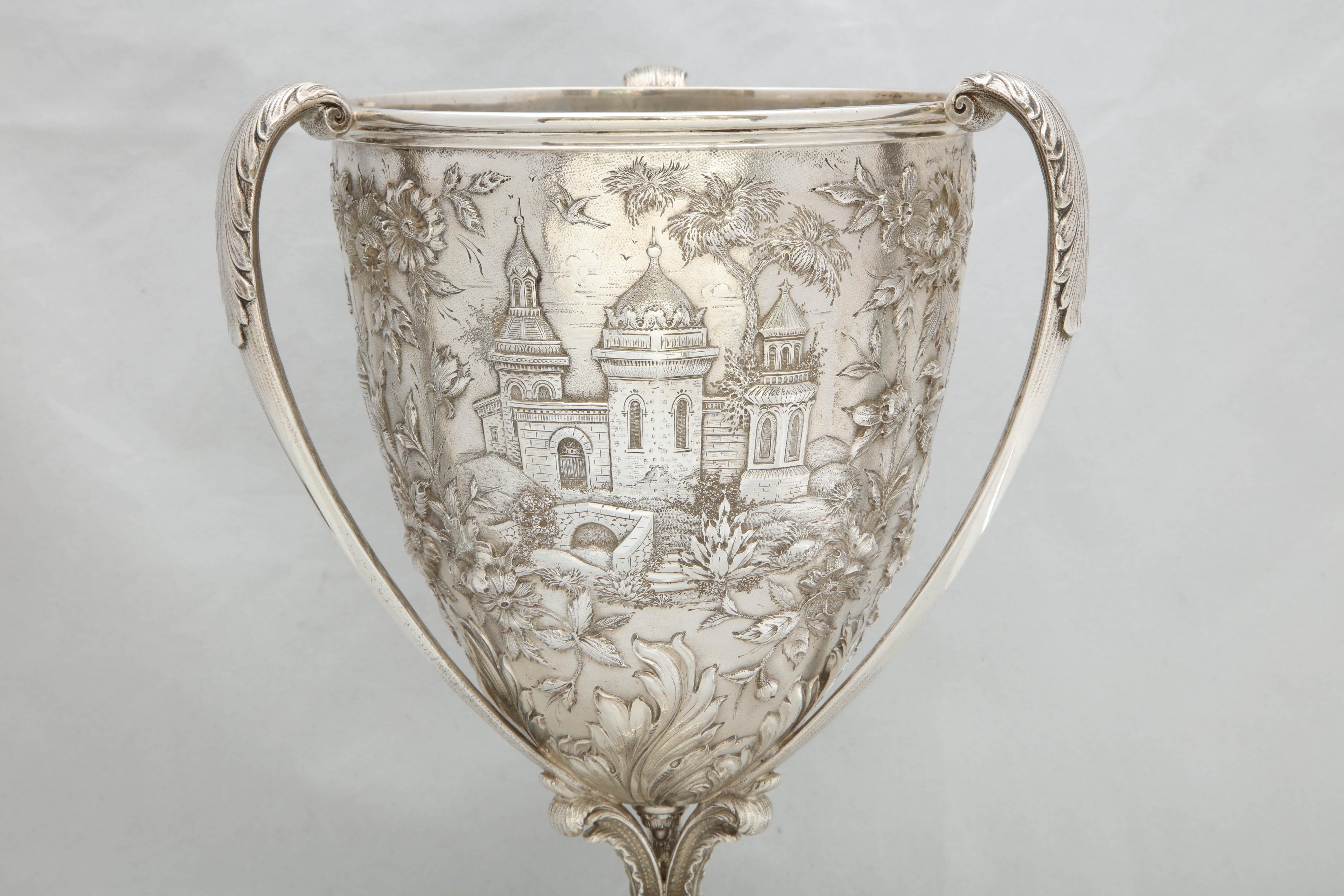 Victorian, sterling silver, three-handled loving cup, S. Kirk and Son, Inc., Baltimore, Maryland, circa 1880s. Chased with architectural scenes. Pedestal base. Measures 12 1/2 inches high x 7 inches diameter across opening x 8 inches wide from