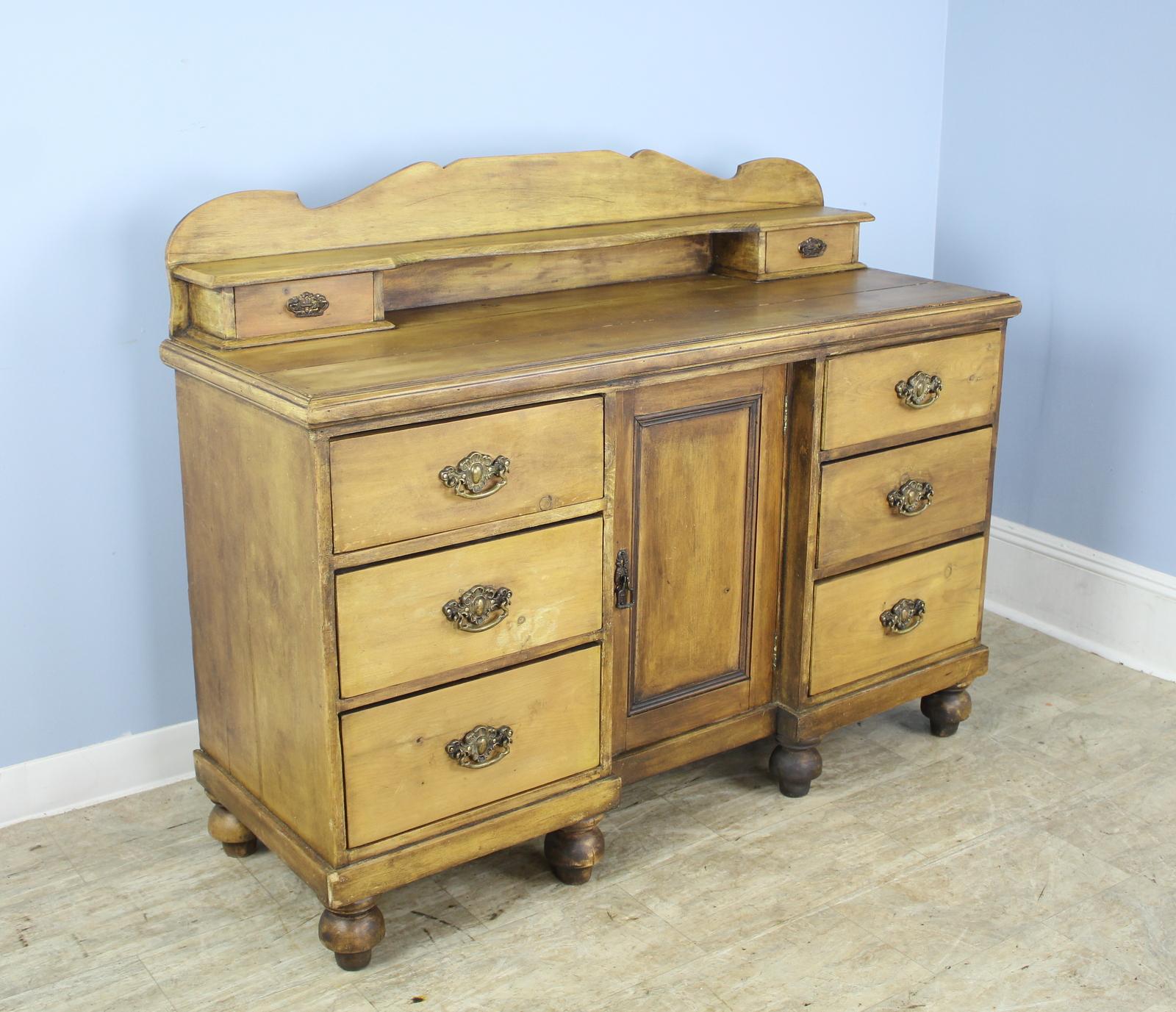 A highly versatile Victorian sideboard, cupboard or buffet. Original yellow paint has been rubbed back for a clean look. Six deep roomy drawers and a center cupboard provides excellent storage, all with charming brass handles. A fixed raised back