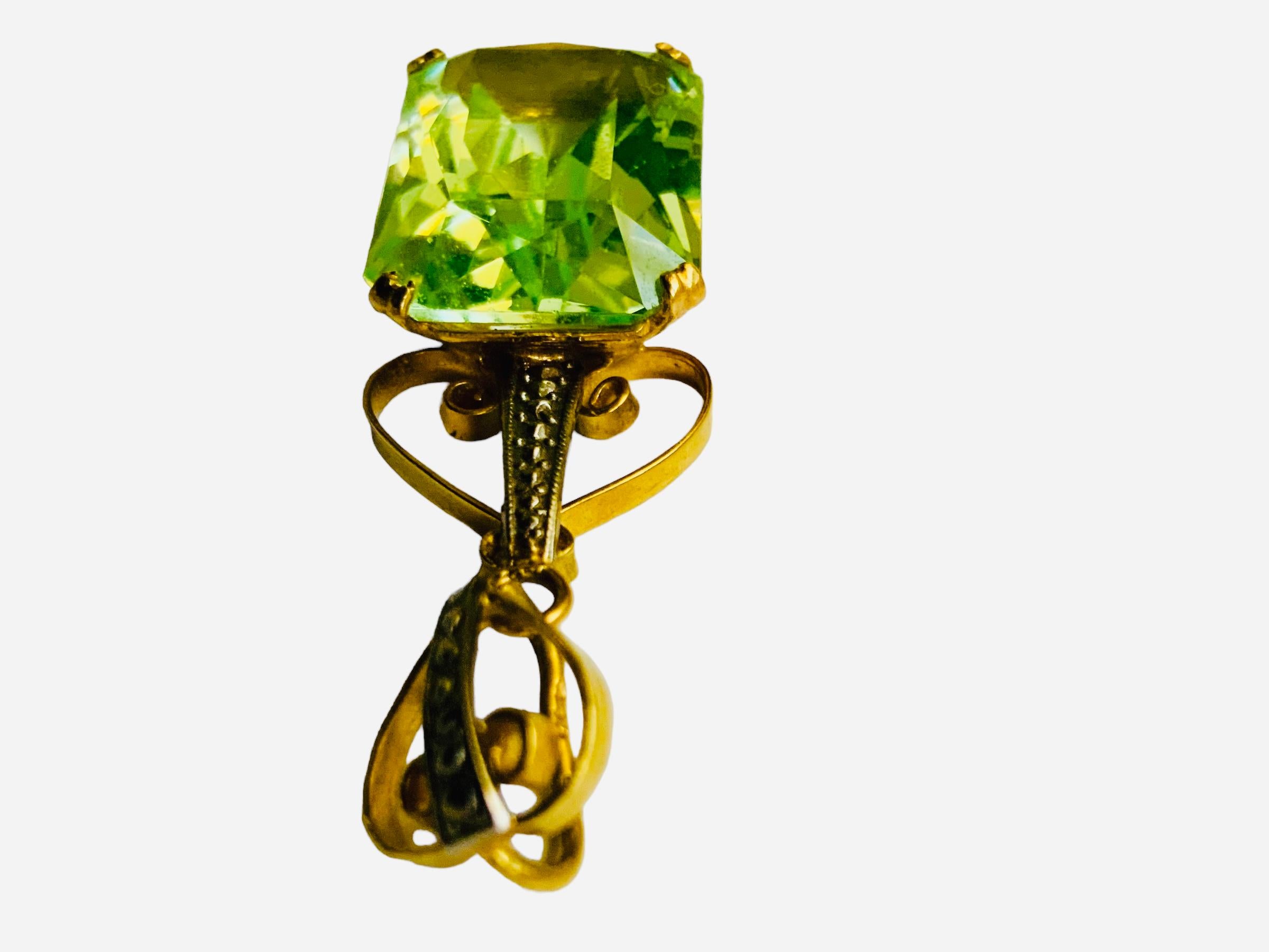 This is a Victorian style 18K yellow Gold Green Topaz Pendant. The Green topaz is emerald cut. It is mounted in a 18K gold rectangular base decorated in their sides with engraved squares with scrolls in their center. The pendant is adorned at the