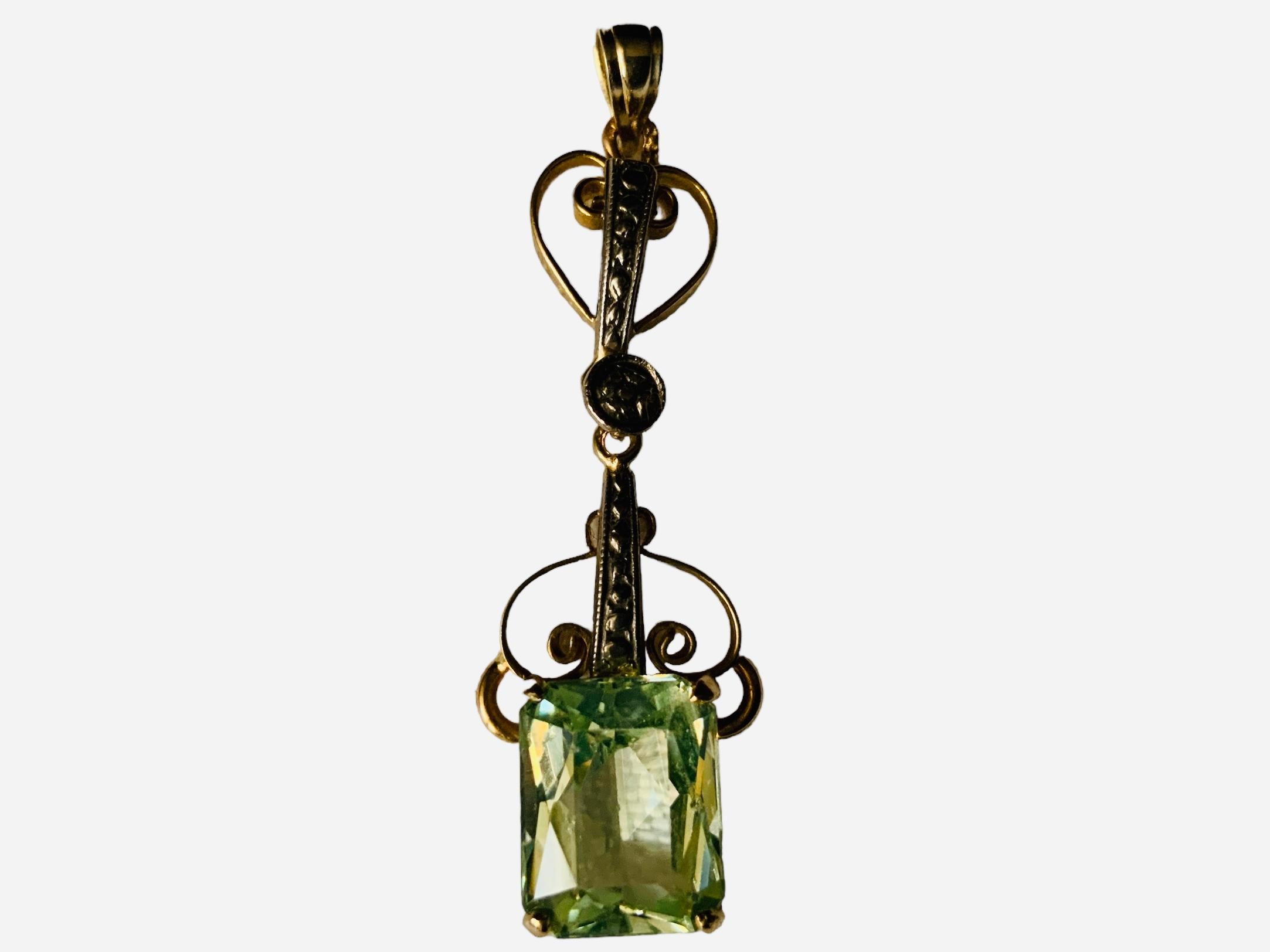 This is a Victorian style 18K yellow Gold light Green topaz Pendant. The light green topaz is emerald cut. It is mounted in a 18K gold rectangular base decorated in their sides with engraved squares with scrolls in their center. The pendant is