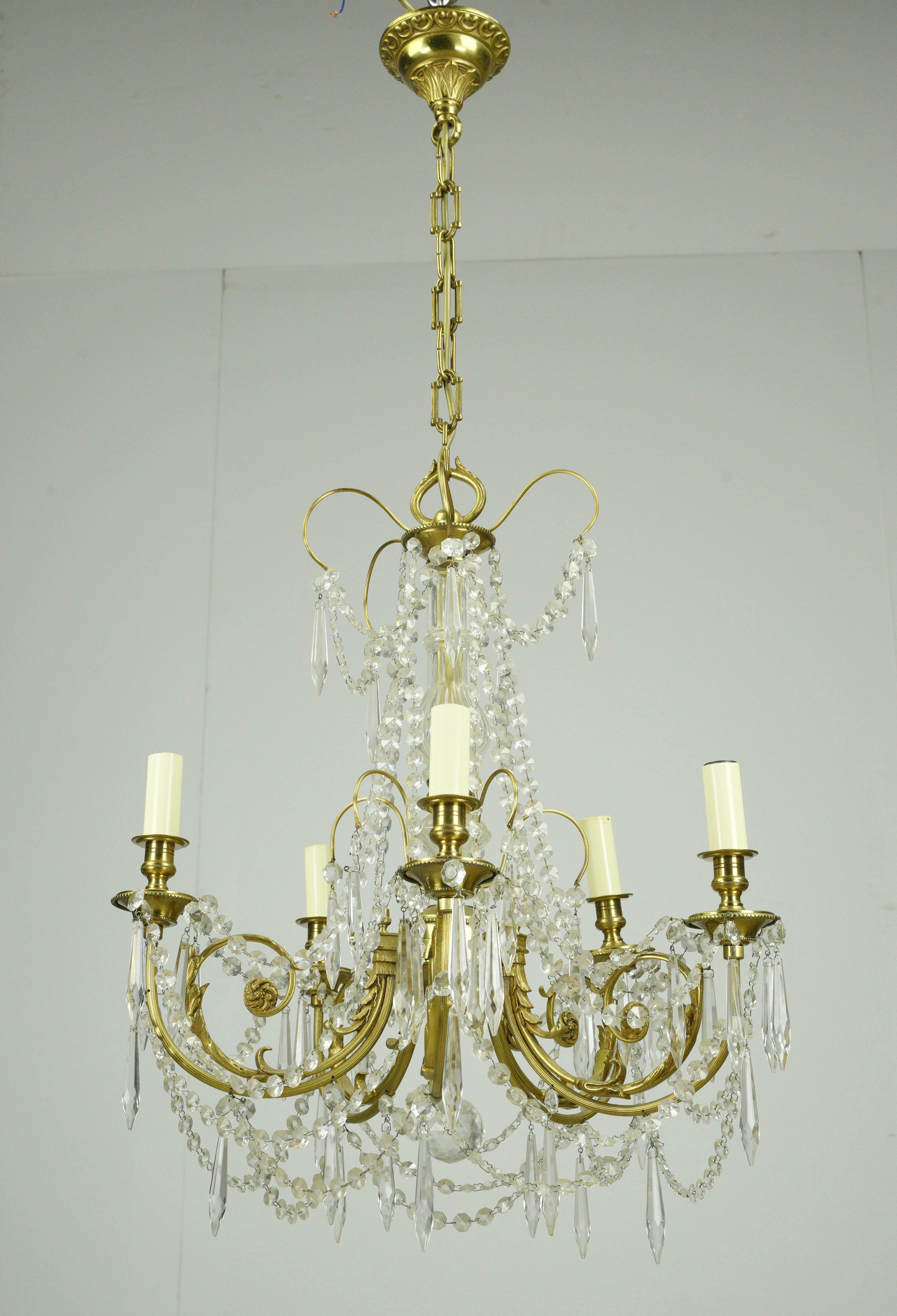 This lighting fixture captures the essence of Victorian design, featuring brass arms. The chandelier is adorned with draped crystal strands and icicle crystals with five arms, each holding a candle style light. This is in good condition with