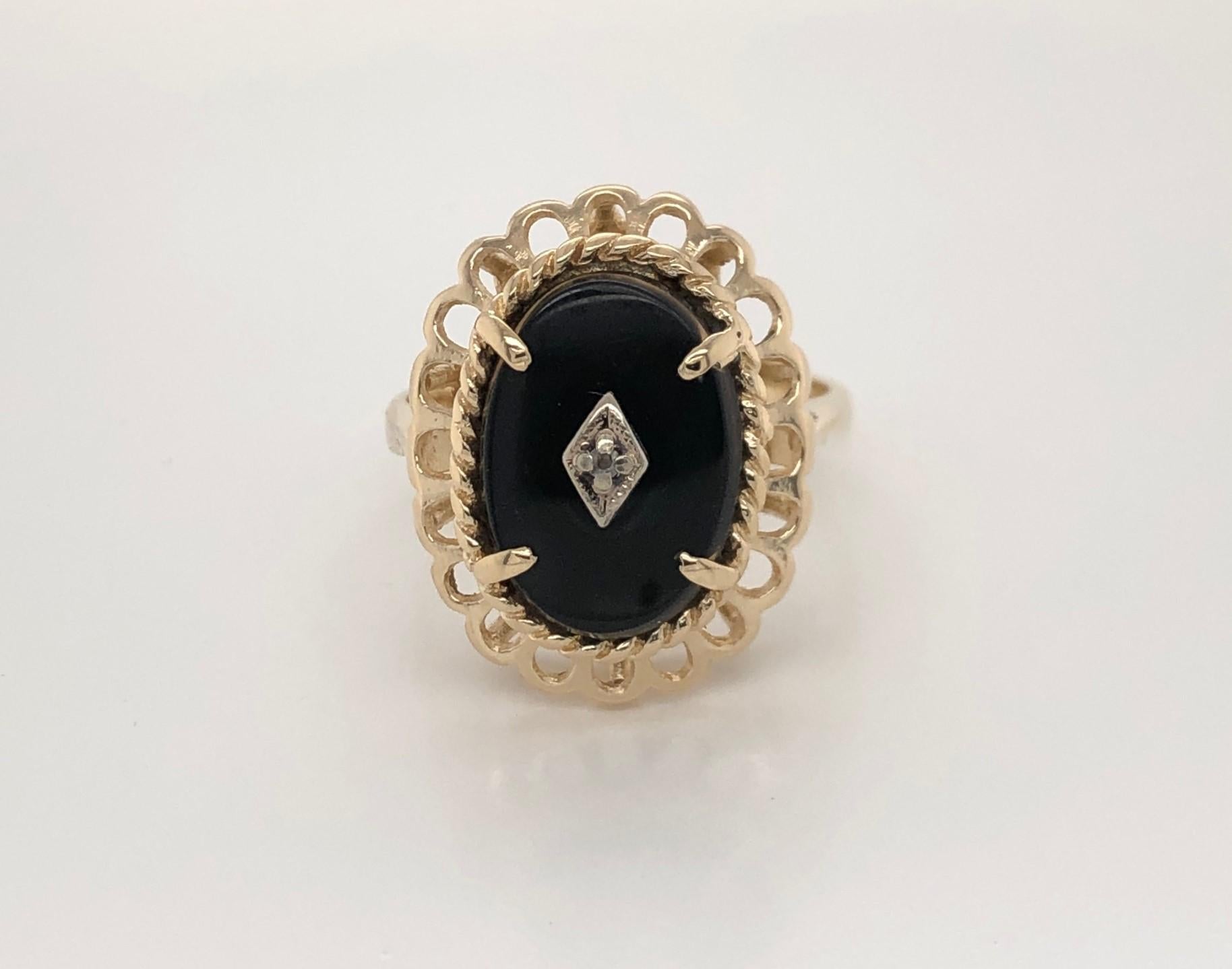 An oval cut black onyx stone enhanced with a center diamond accent makes a strong presentation outlined in polished fourteen carat  lacy filigree border. In size 7, with the head measuring approximately 20.5 mm x 16.5 mm, this quality ring created