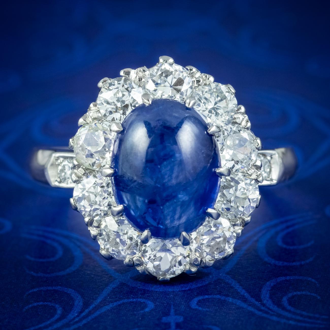 Ein hervorragender, viktorianisch inspirierter Ring mit einem verführerischen blauen Cabochon-Saphir als Herzstück, umgeben von zehn leuchtenden Diamanten im alten europäischen Schliff am Rand und einem weiteren auf jeder Schulter.

Das Stück wird